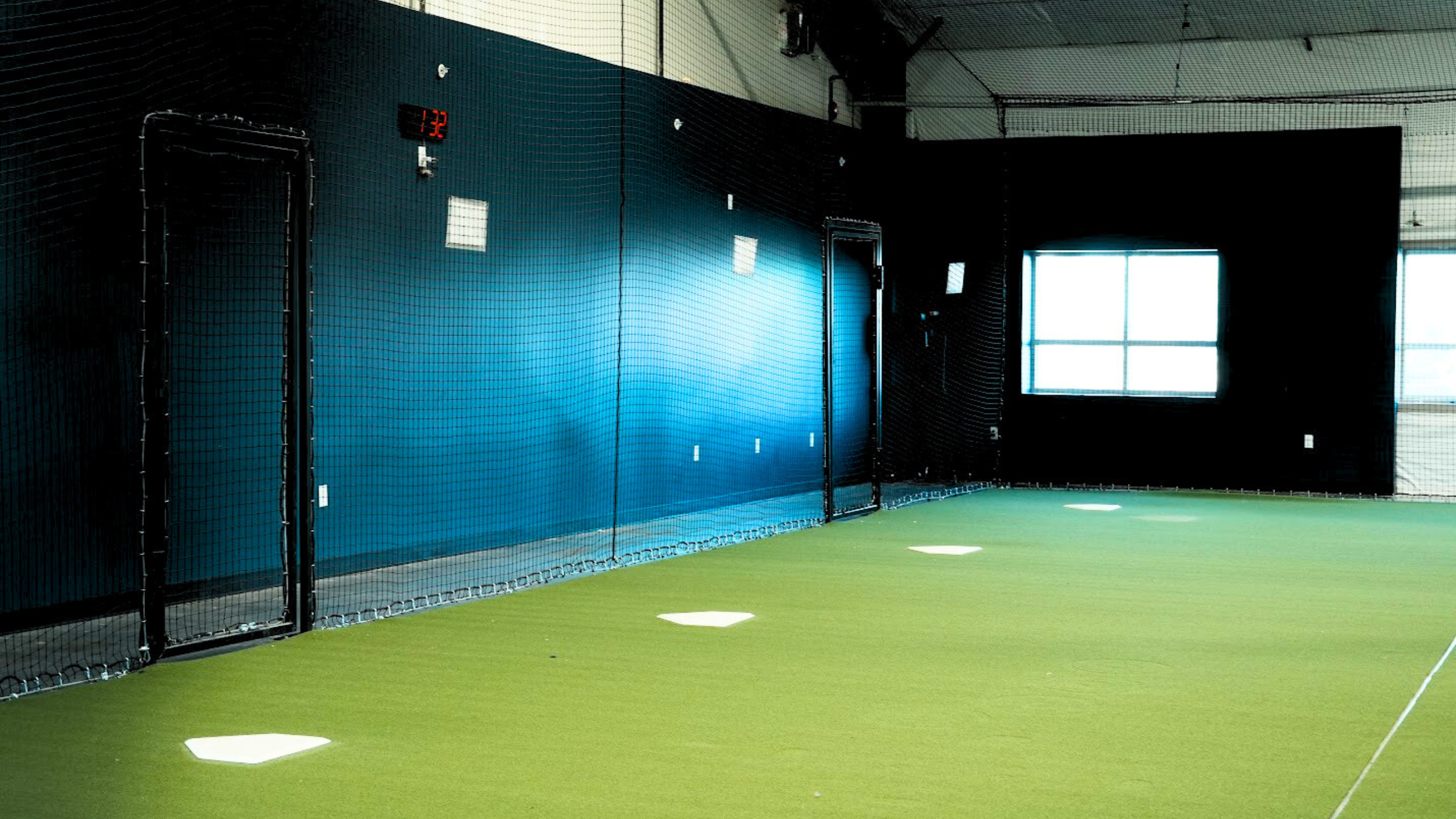 Indoor batting cage with multiple turf lanes and protective netting at The Wave training facility Waverly Nebraska