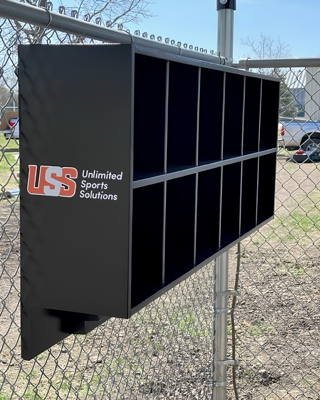 USS branded black dugout helmet rack mounted on chain link fence