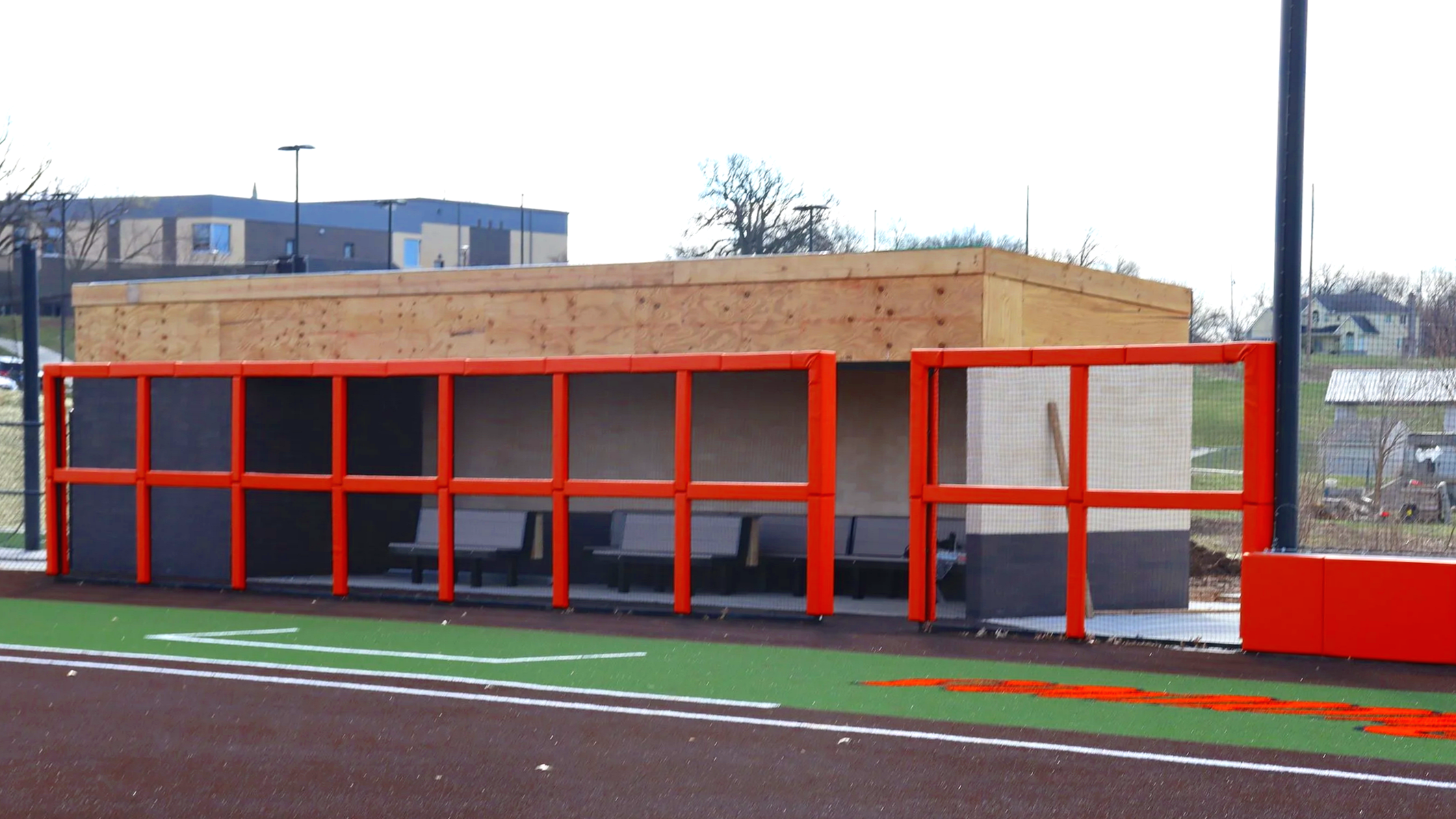 Dugout rail padding and exterior wall padding installed on new orange and grey baseball dugout at Bonner Springs athletic facility on synthetic turf field — USS sports field padding supplier