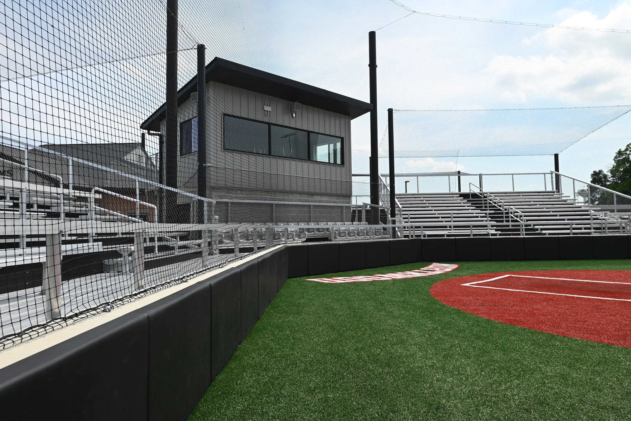 College baseball facility with press box, aluminum bleachers, and outfield wall padding