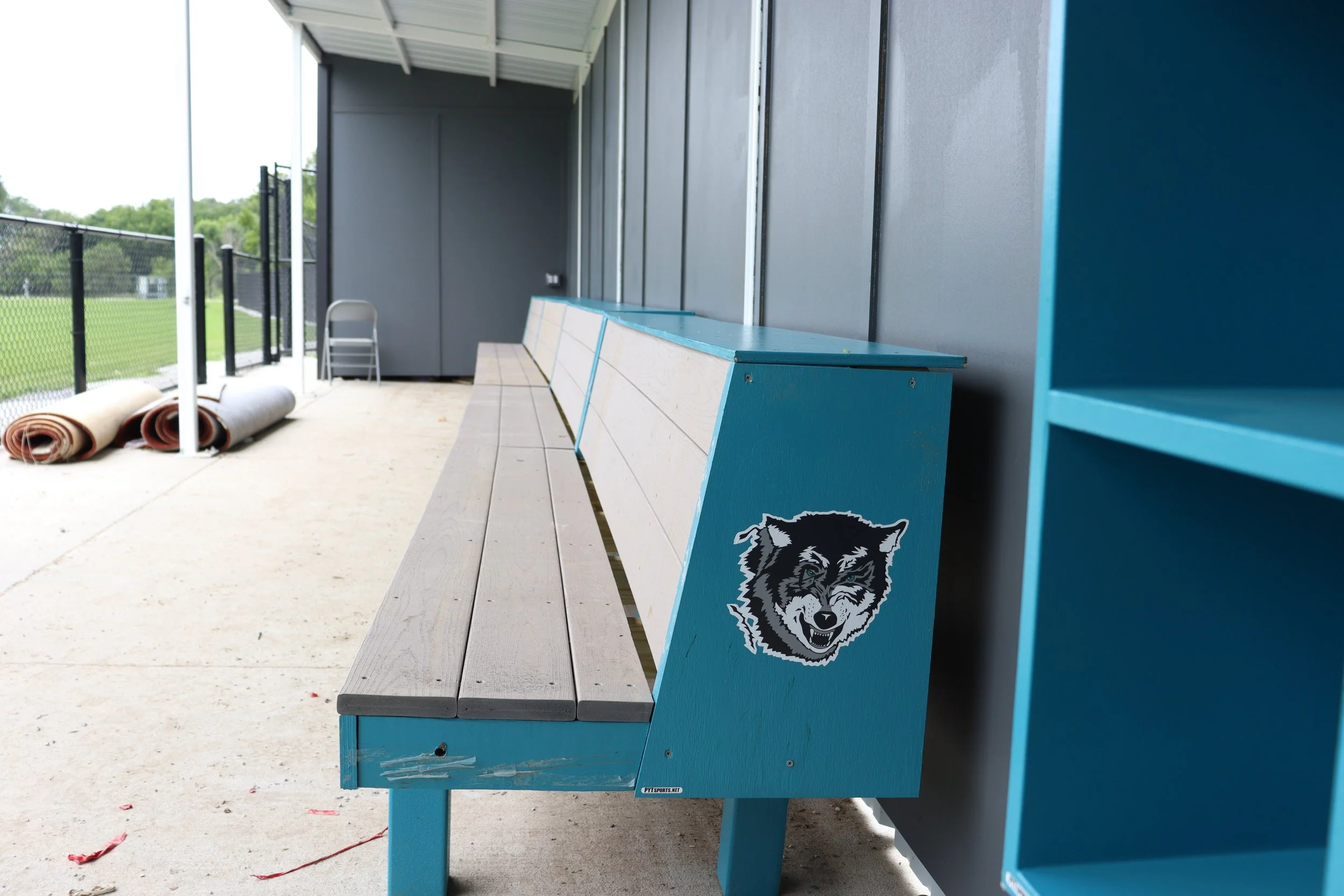 Custom teal painted Pro bench with school mascot branding inside high school athletic facility dugout — USS athletic facility benches supplier for high school sports programs