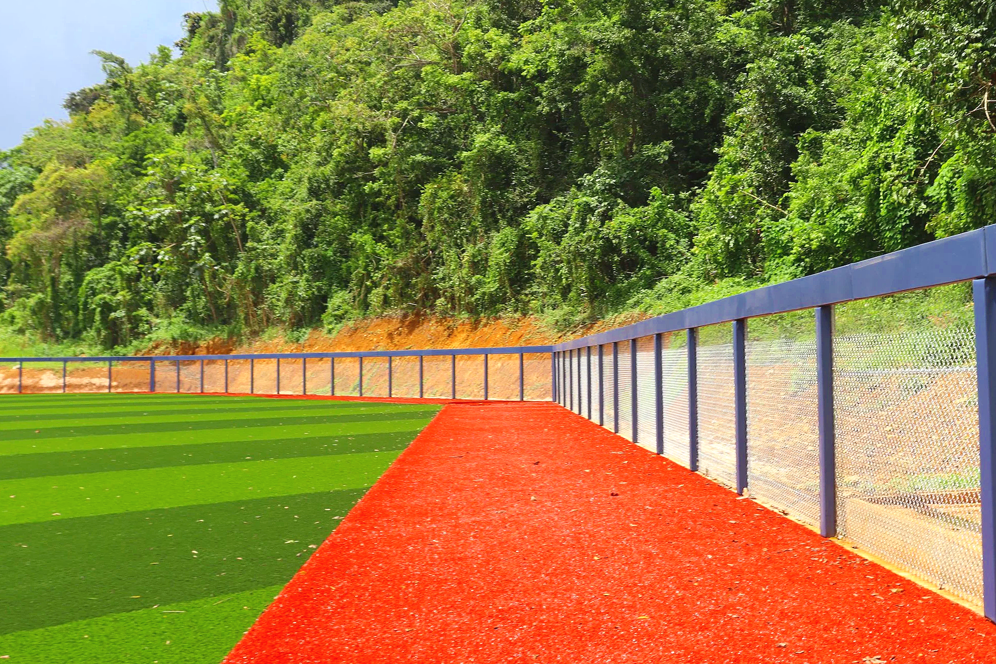 Blue post and rail padding installed along outfield fence top rail and seams on professional synthetic turf baseball field with red warning track — USS sports field padding supplier