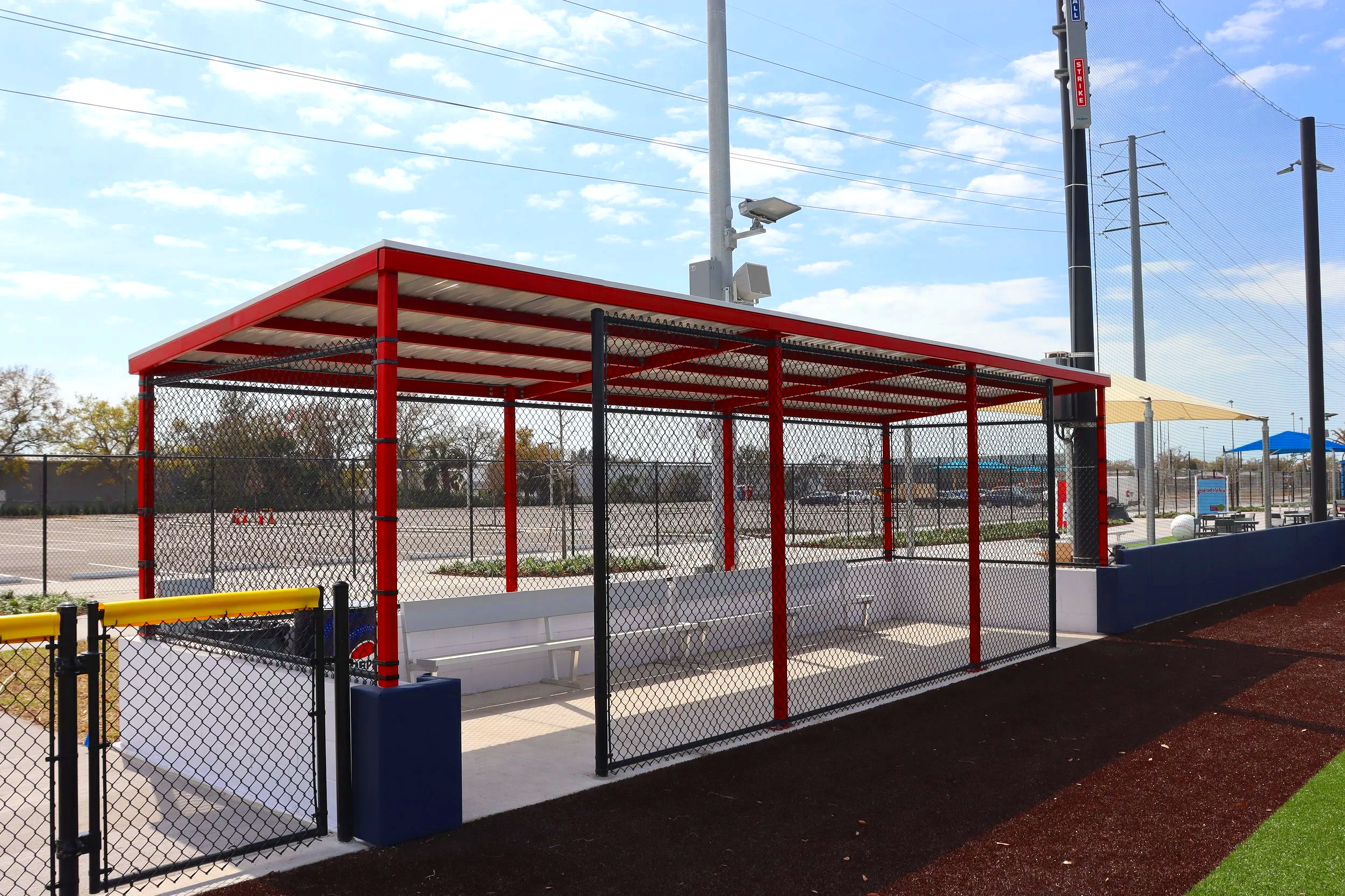 Red and black covered dugout structure with bench seating at athletic complex tournament facility — USS athletic facility benches and dugout supplier for sports complexes and tournament venues
