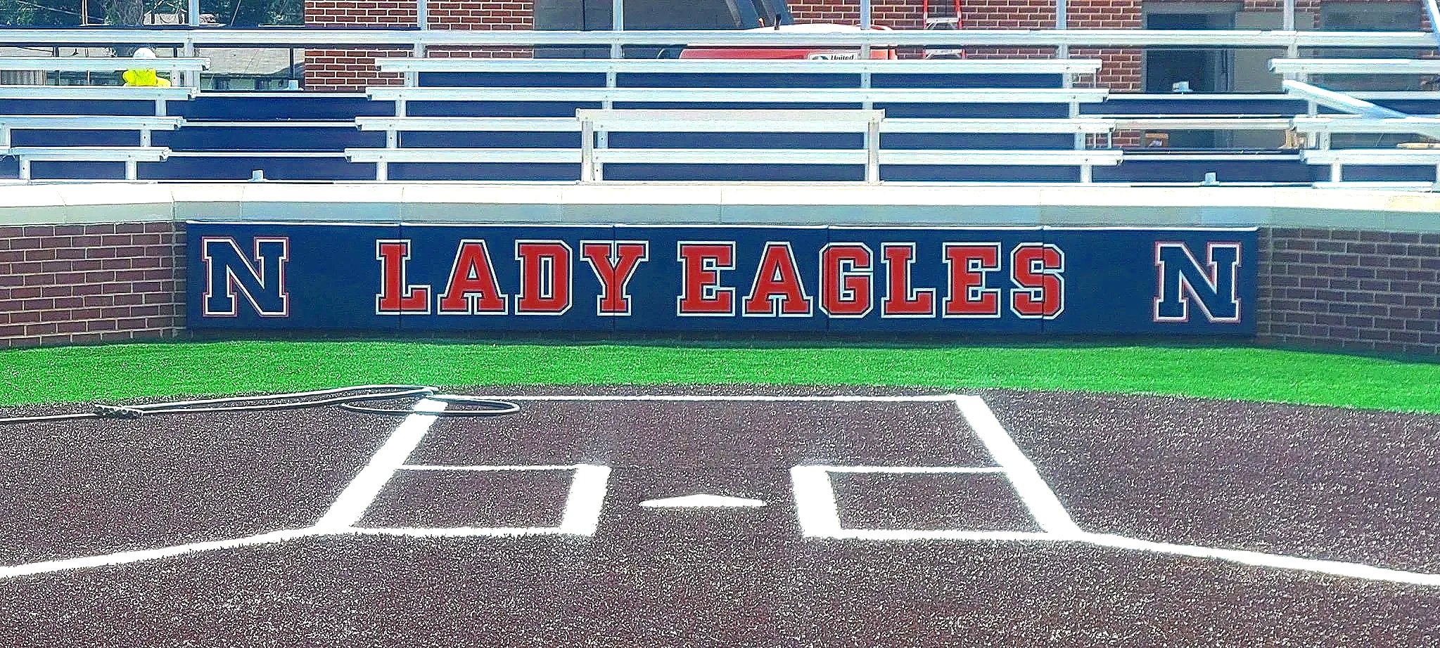 Custom Lady Eagles branded padding panels on softball dugout wall with bleachers