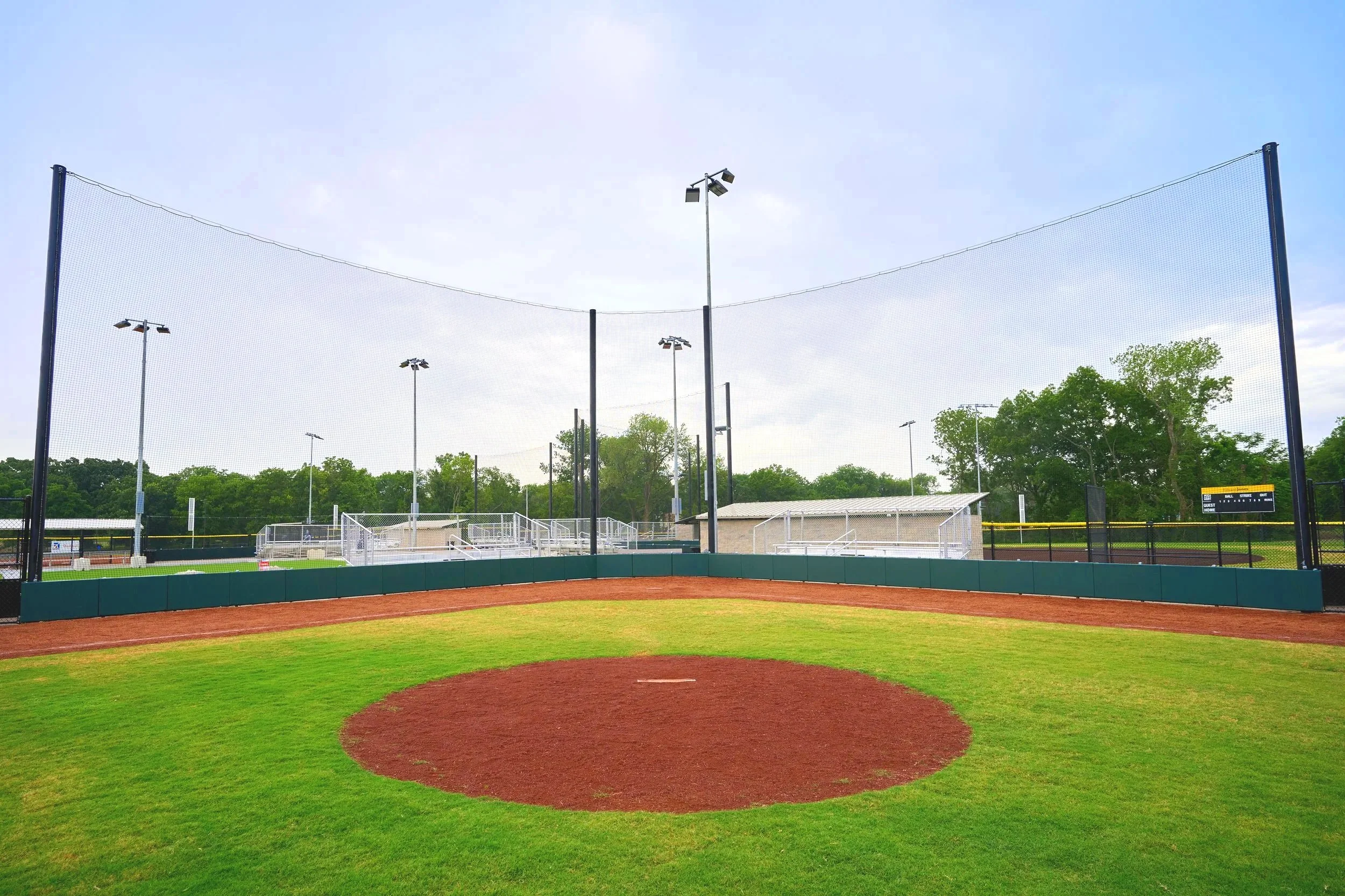 Portable pitching mound on natural grass baseball field with barrier netting dugouts bleachers and stadium lighting — USS portable pitching mound supplier
