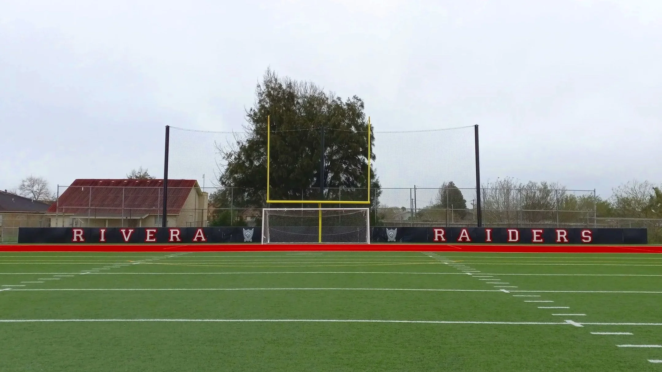 Soccer goal on artificial turf field with branded wall padding at Rivera Raiders athletic facility