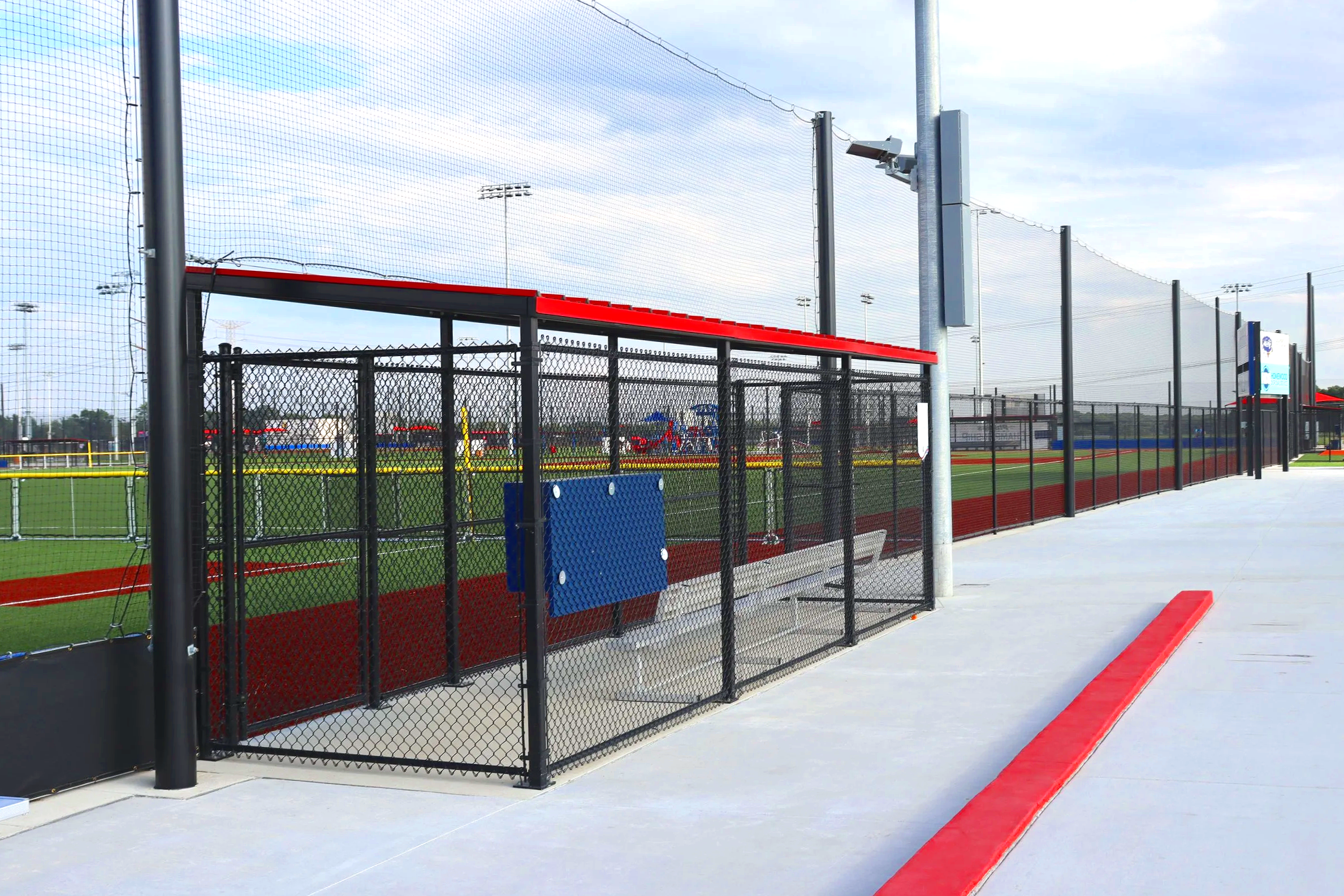 Fielder's Choice PRO baseball dugout with red metal roof bench seating and barrier netting at Crossroads athletic facility in New Lenox Illinois — USS baseball dugout supplier
