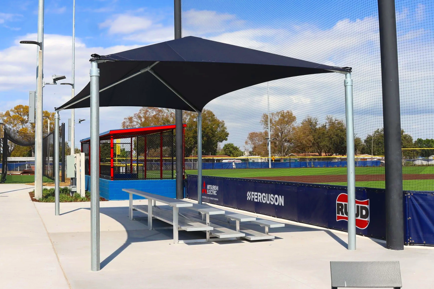 Sponsored bleacher wrap with Ferguson and RUD branding at baseball complex with hip shade structure