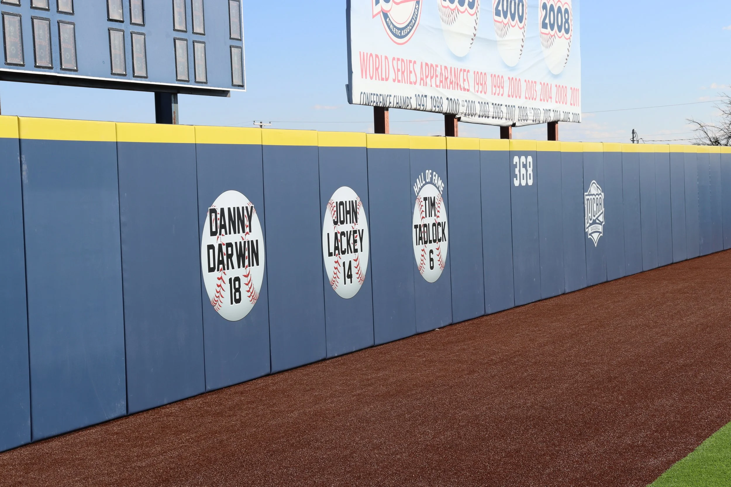 Custom Hall of Fame retired number graphics on outfield wall padding at professional baseball tournament complex