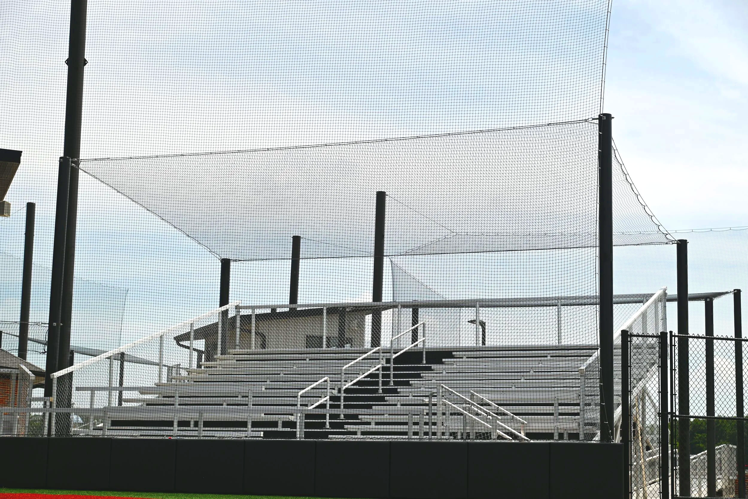  Aluminum bleachers lining both sides of a softball field with safety netting and press box — USS aluminum bleachers supplier for high school athletic facilities and sports complexes