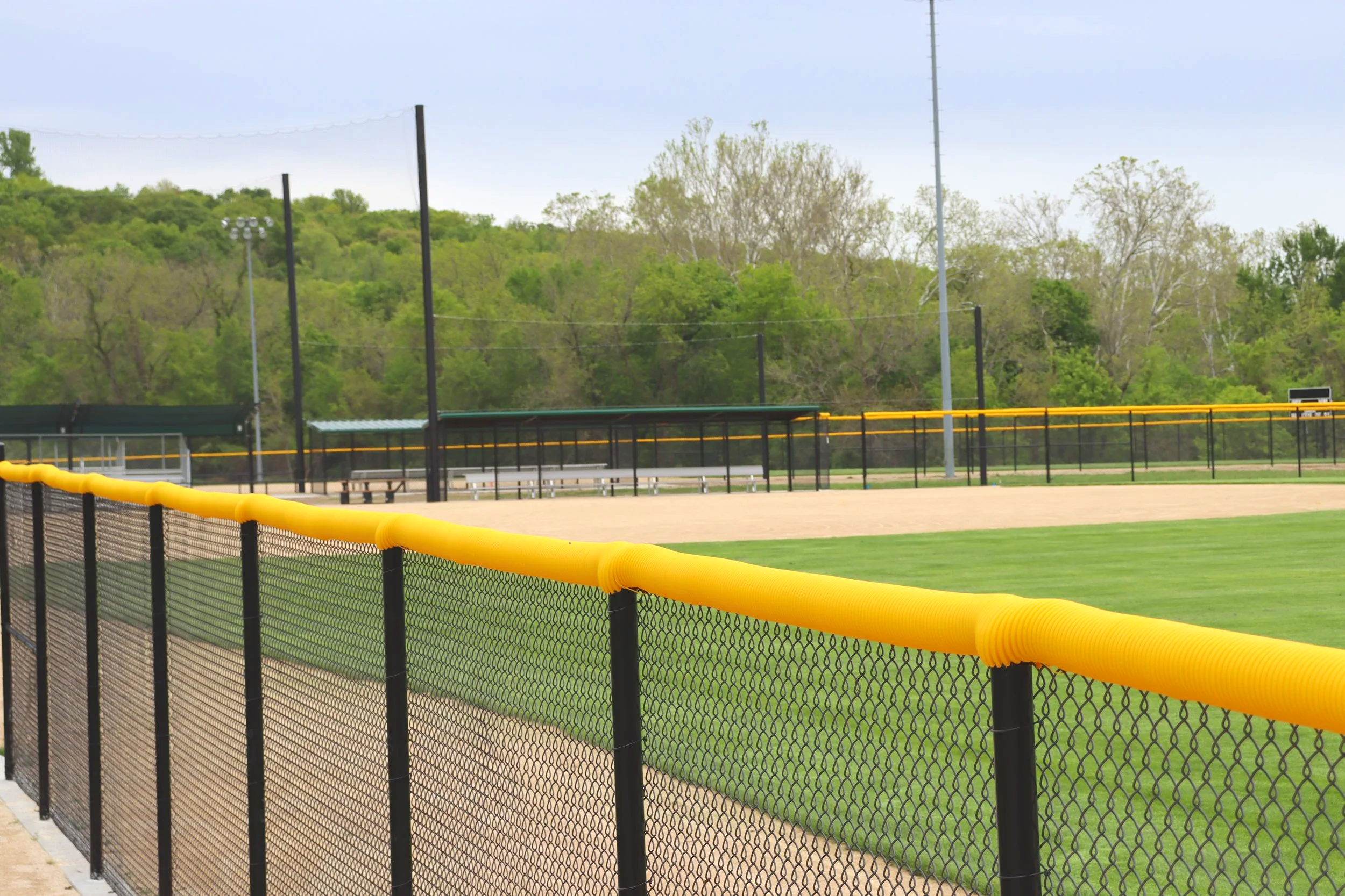 Yellow fence cap on black chain link outfield fence at baseball facility