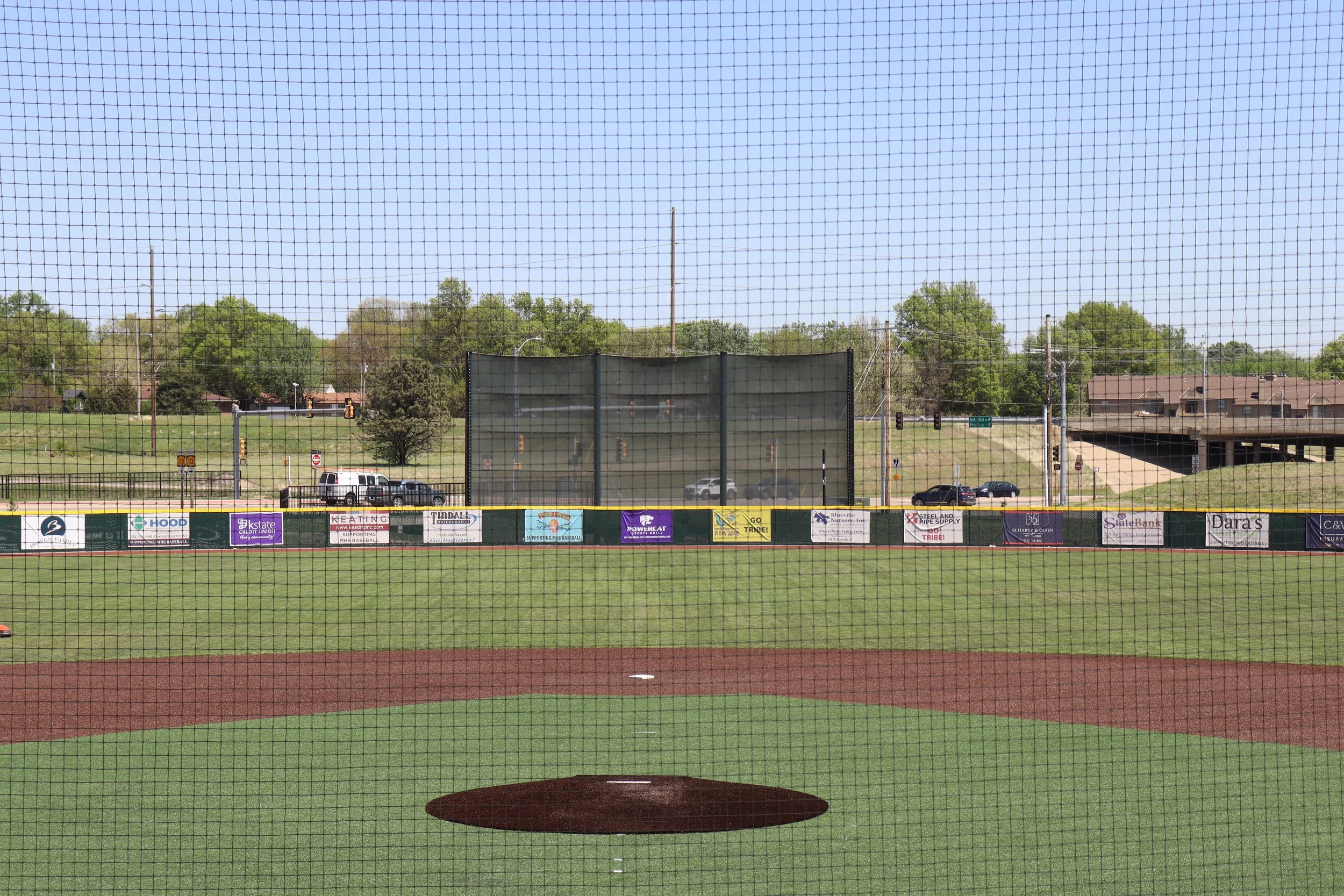 Batter's eye backdrop in center field at baseball complex with sponsor fence signage and backstop netting