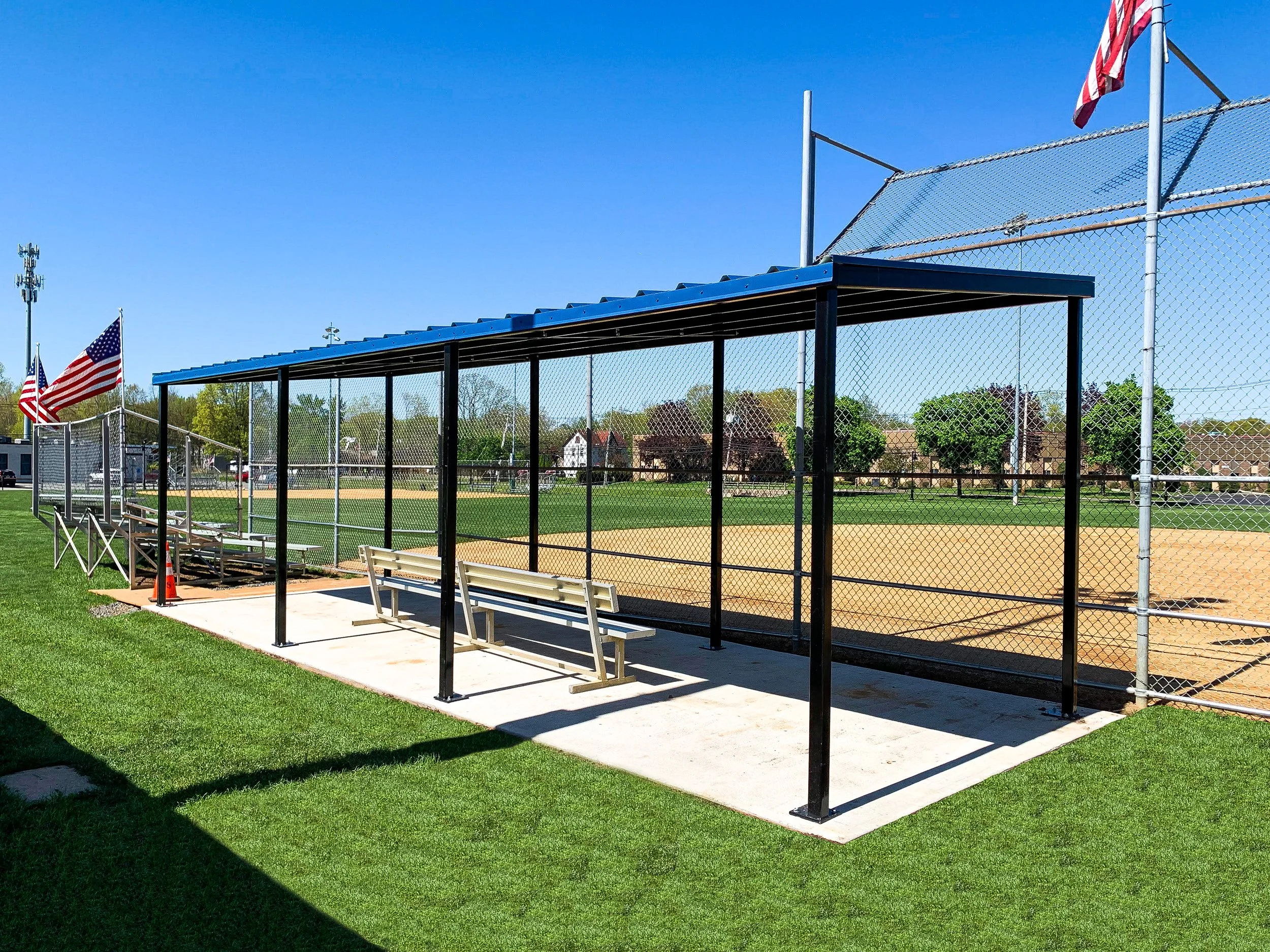 High school baseball dugout with blue roof and chain link fencing on artificial turf field
