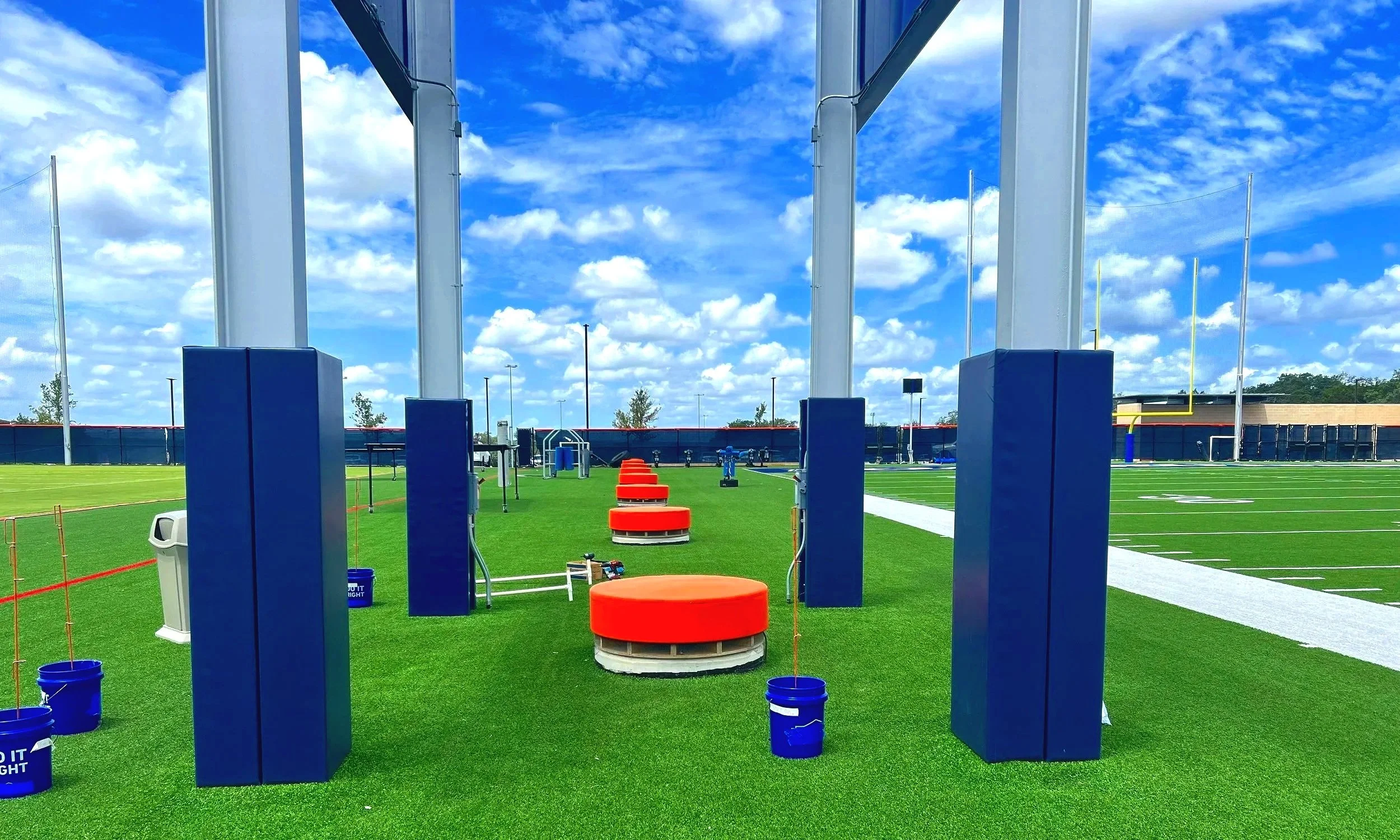 Blue post and column padding on structural supports with orange sideline surface padding on synthetic turf at professional football practice facility — USS sports field padding supplier
