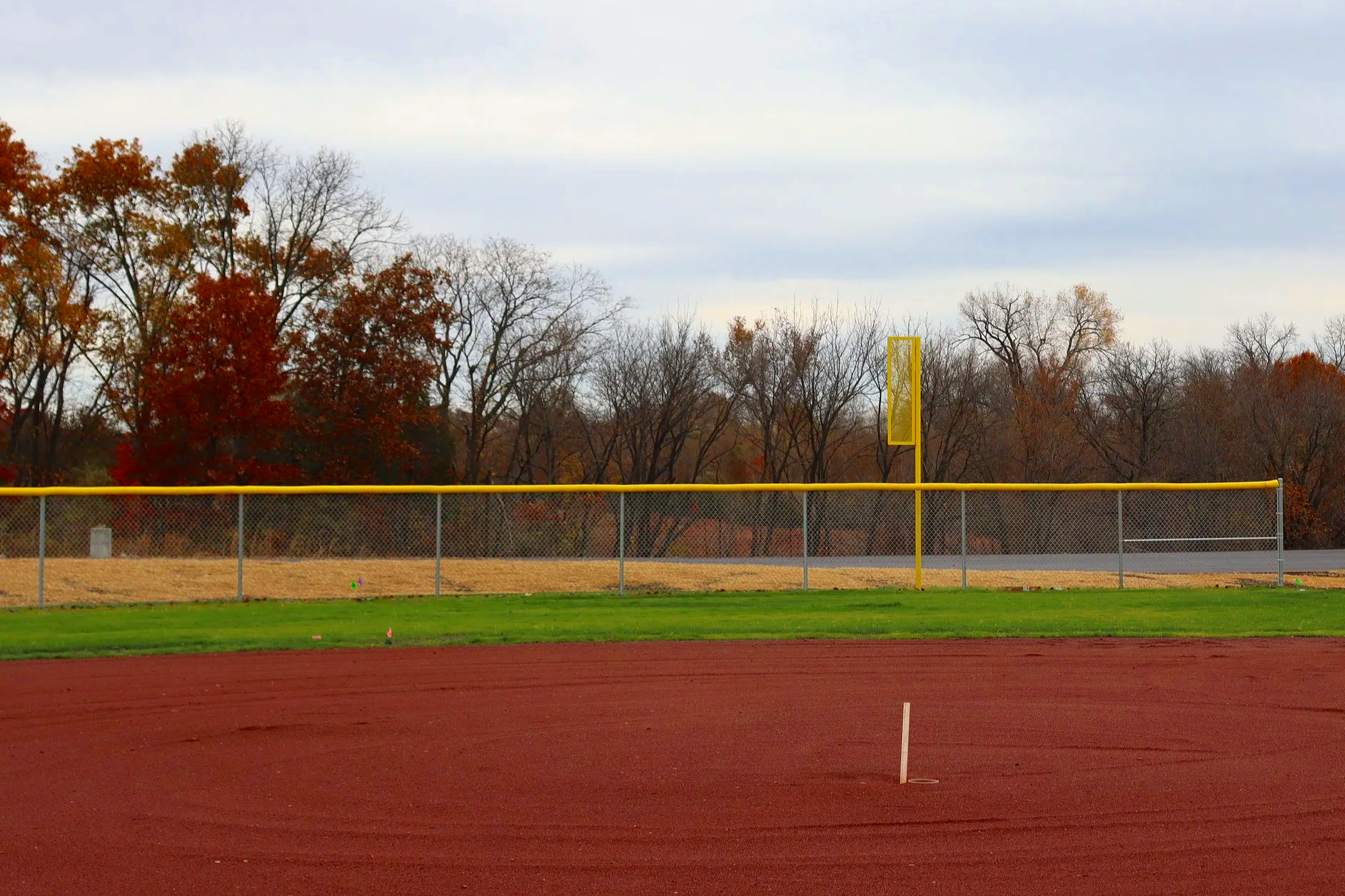  Yellow fence cap on chain link outfield fence with foul pole at baseball field, fall season