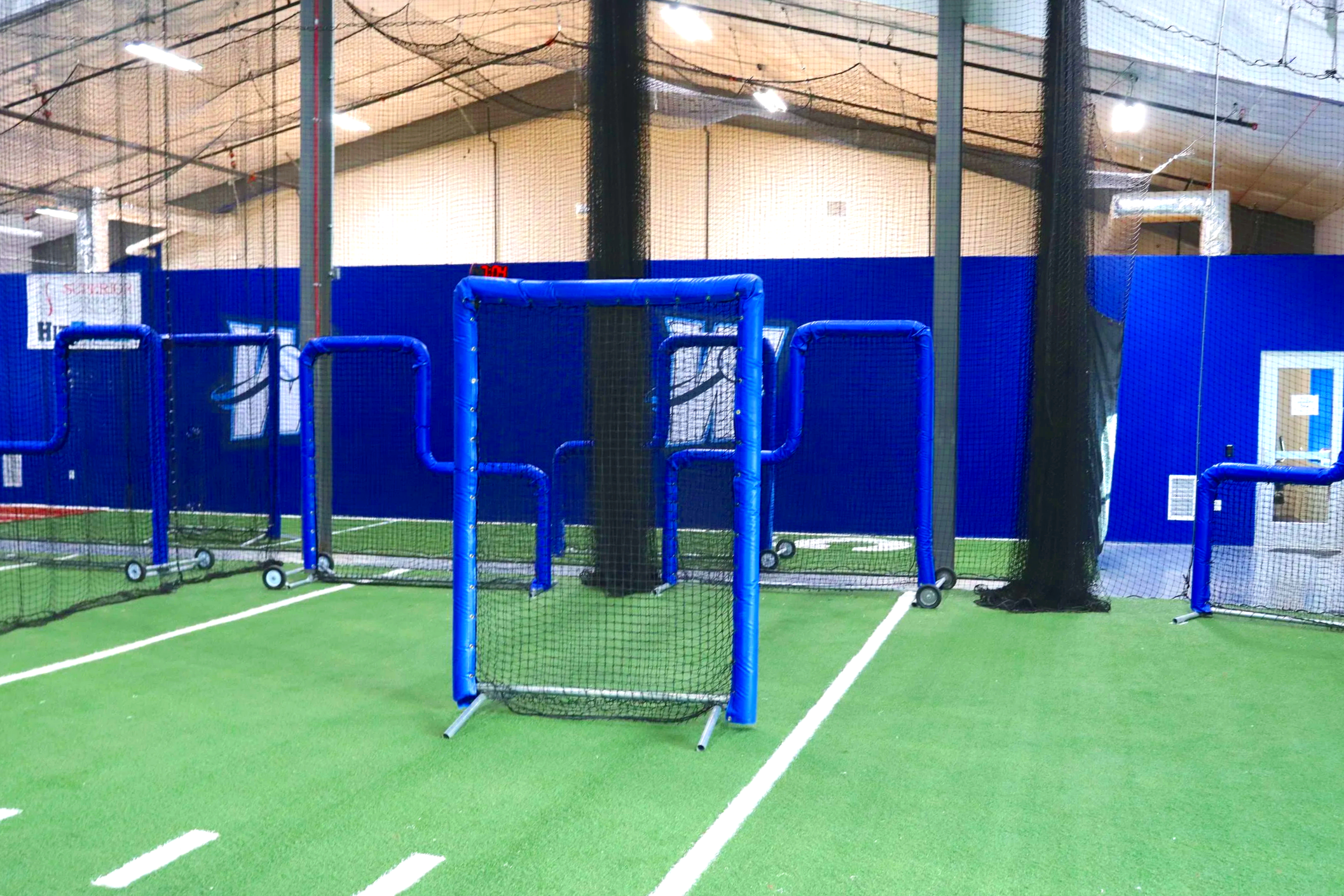 Blue indoor athletic facility wall padding with overhead barrier netting and portable batting cages at The Wave indoor training facility in Waverly Nebraska — USS sports field padding supplier