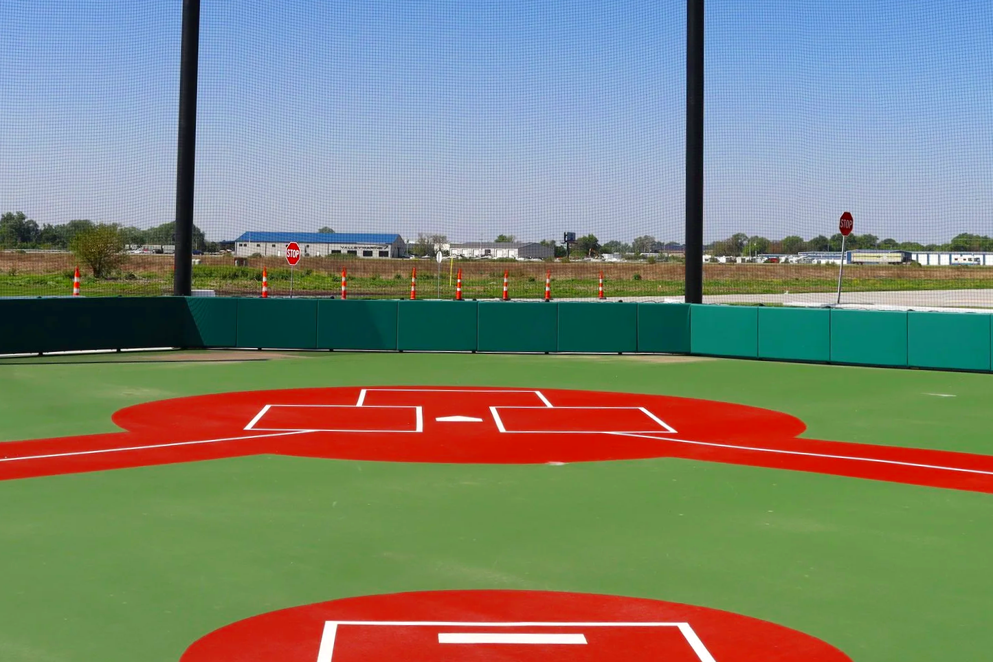 Portable pitching mound on synthetic turf baseball field with green exterior wall padding and barrier netting — USS portable pitching mound supplier