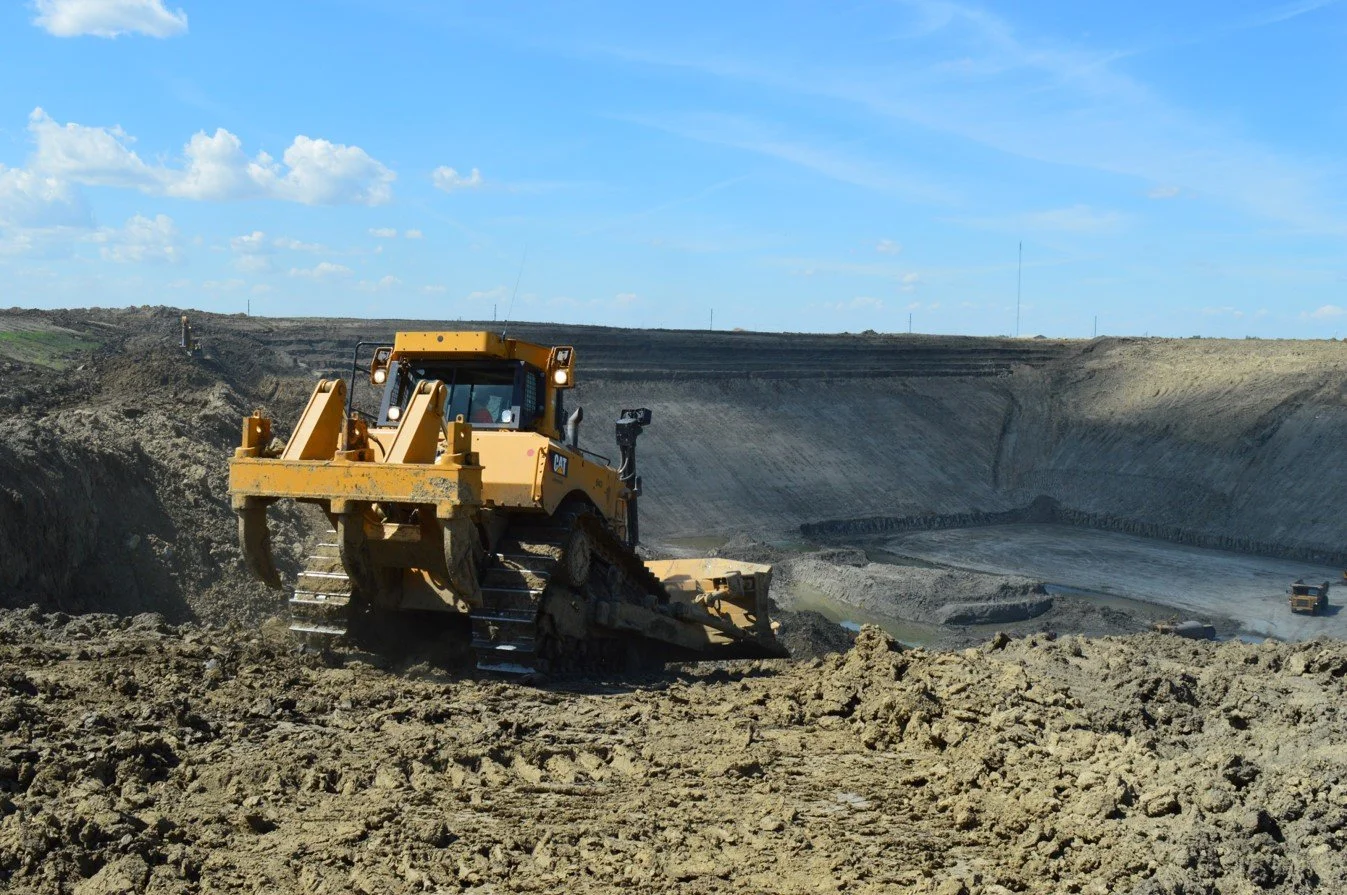 A bulldozer working in an excavated construction site with a large dirt pit, under a partly cloudy sky.