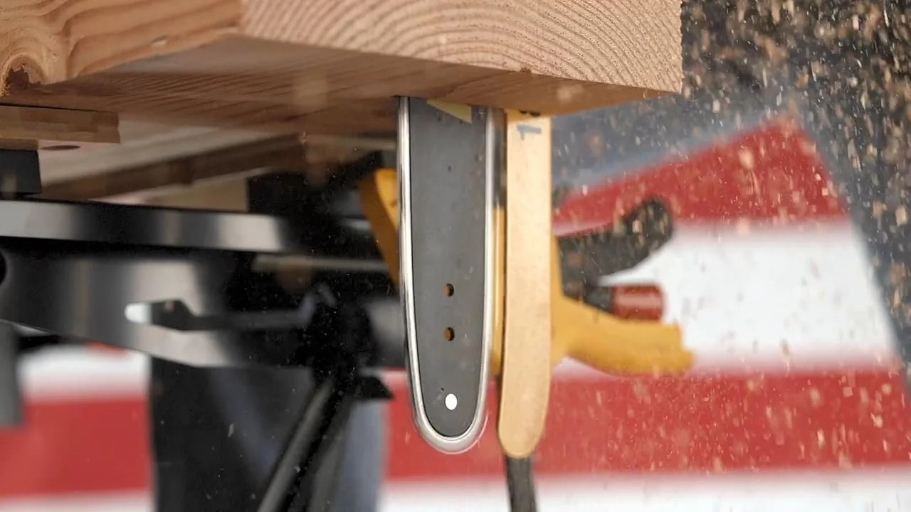 A close-up of a woodworking saw with wood pieces and sawdust around it, placed on a workbench in a woodworking shop.