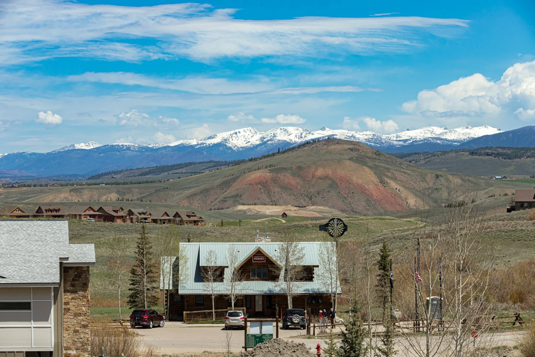 Scenic view of snow-capped mountains in the background, rolling hills and a small town with houses and a commercial building labeled 'HOMES' in the foreground.