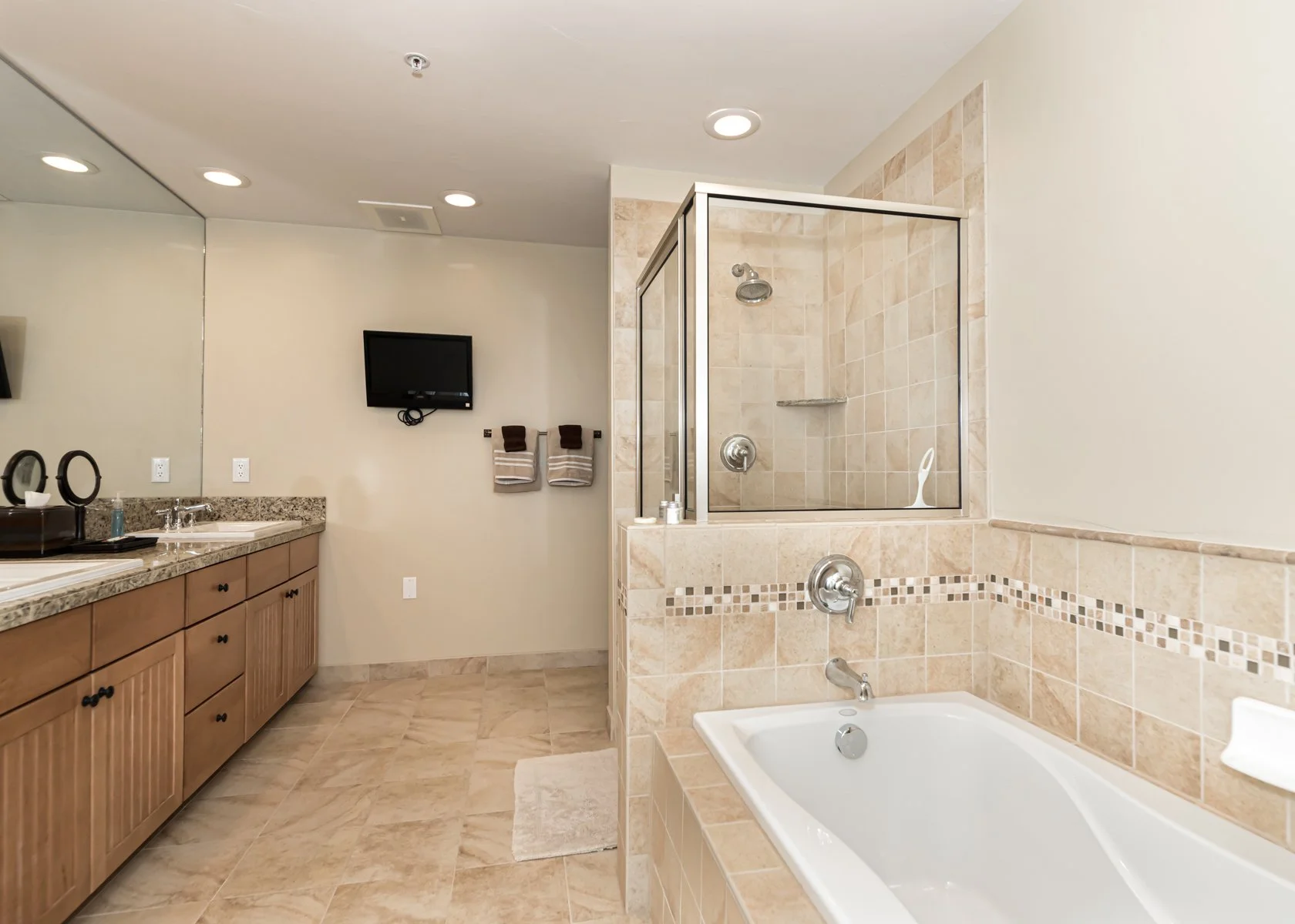 Bathroom with a bathtub, a separate tiled shower stall, a wooden vanity with a granite countertop, a wall-mounted TV, and a mirror.