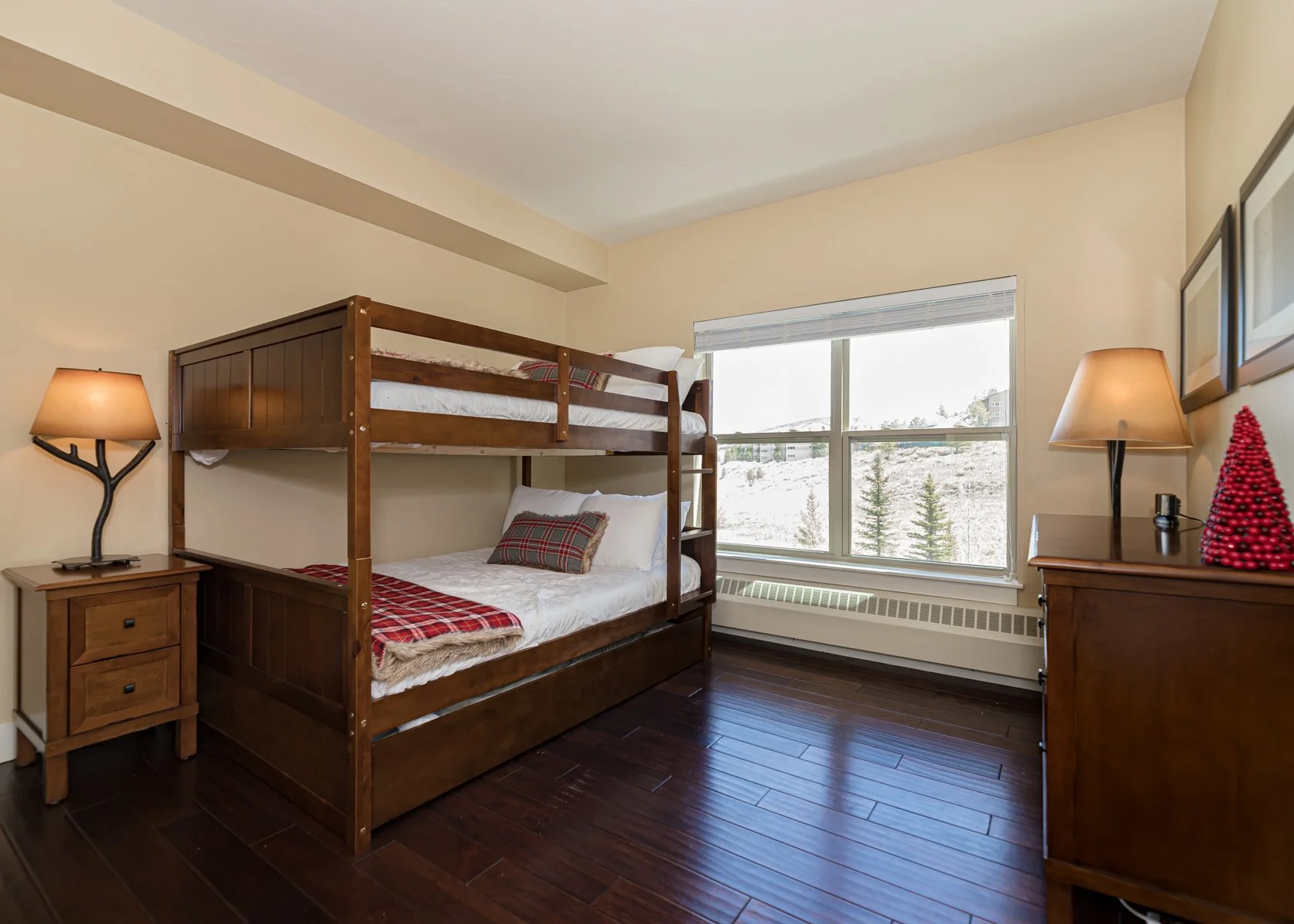 Bedroom with a bunk bed, nightstands with lamps, and a large window showing a snowy landscape outside.
