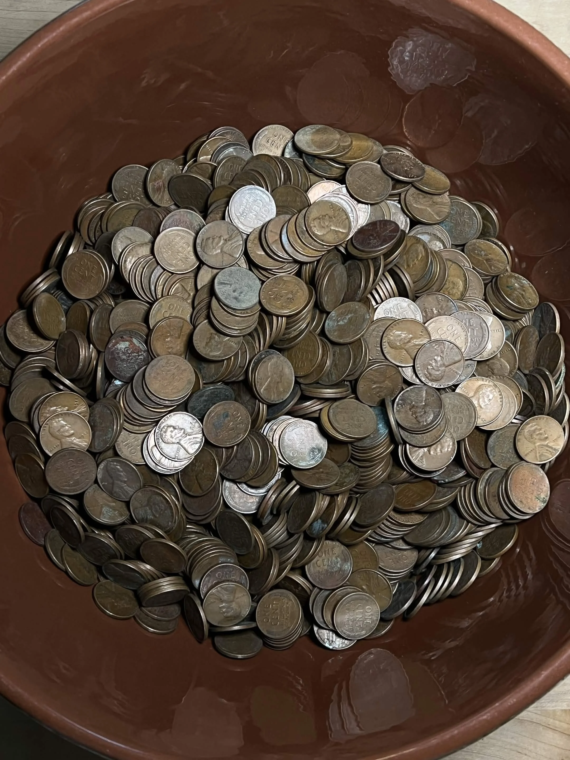 A brown bowl filled with scattered United States one-cent coins.