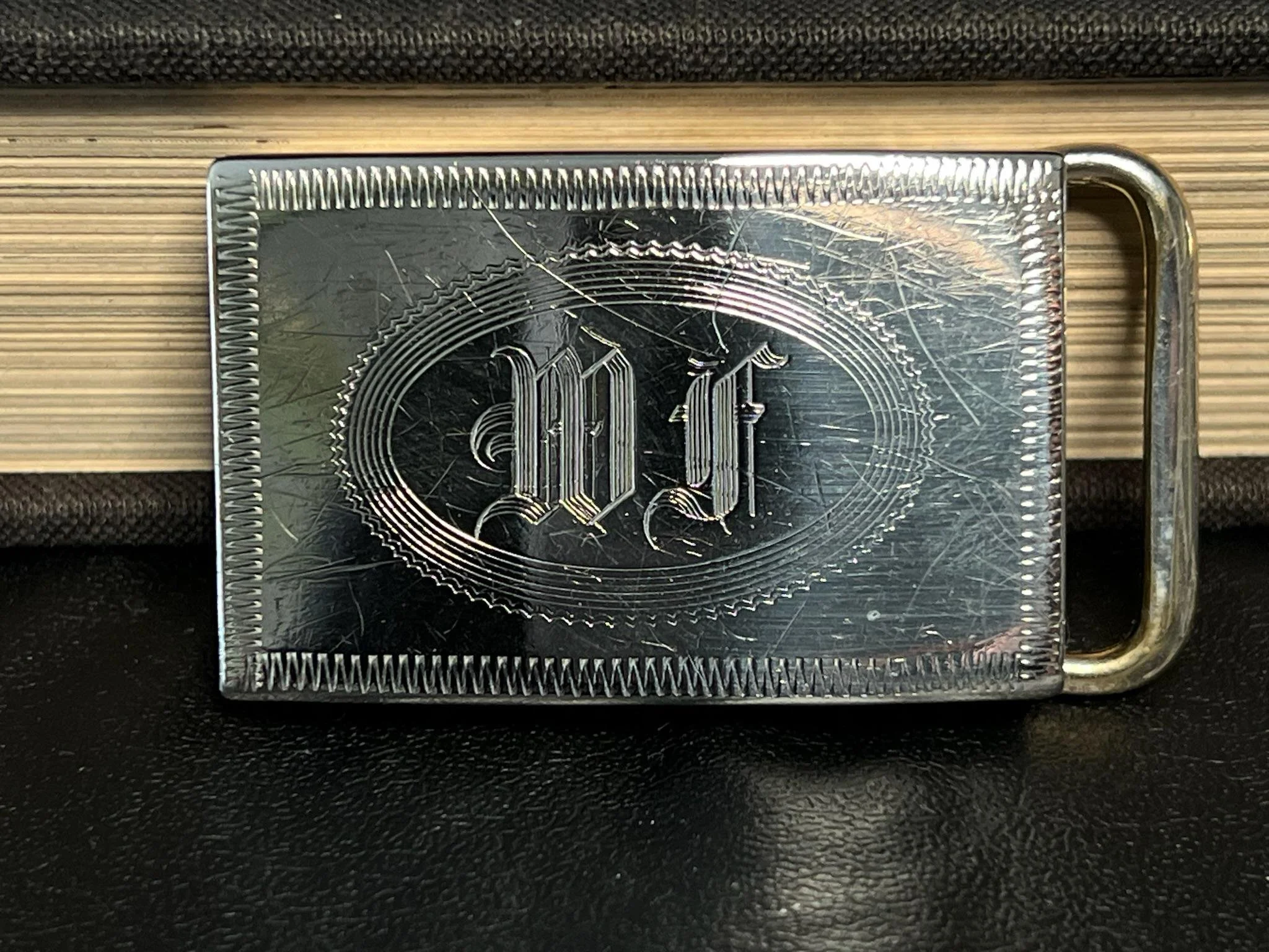 Close-up of a silver metallic keychain with engraved design and the letter 'W', placed on a wooden surface.