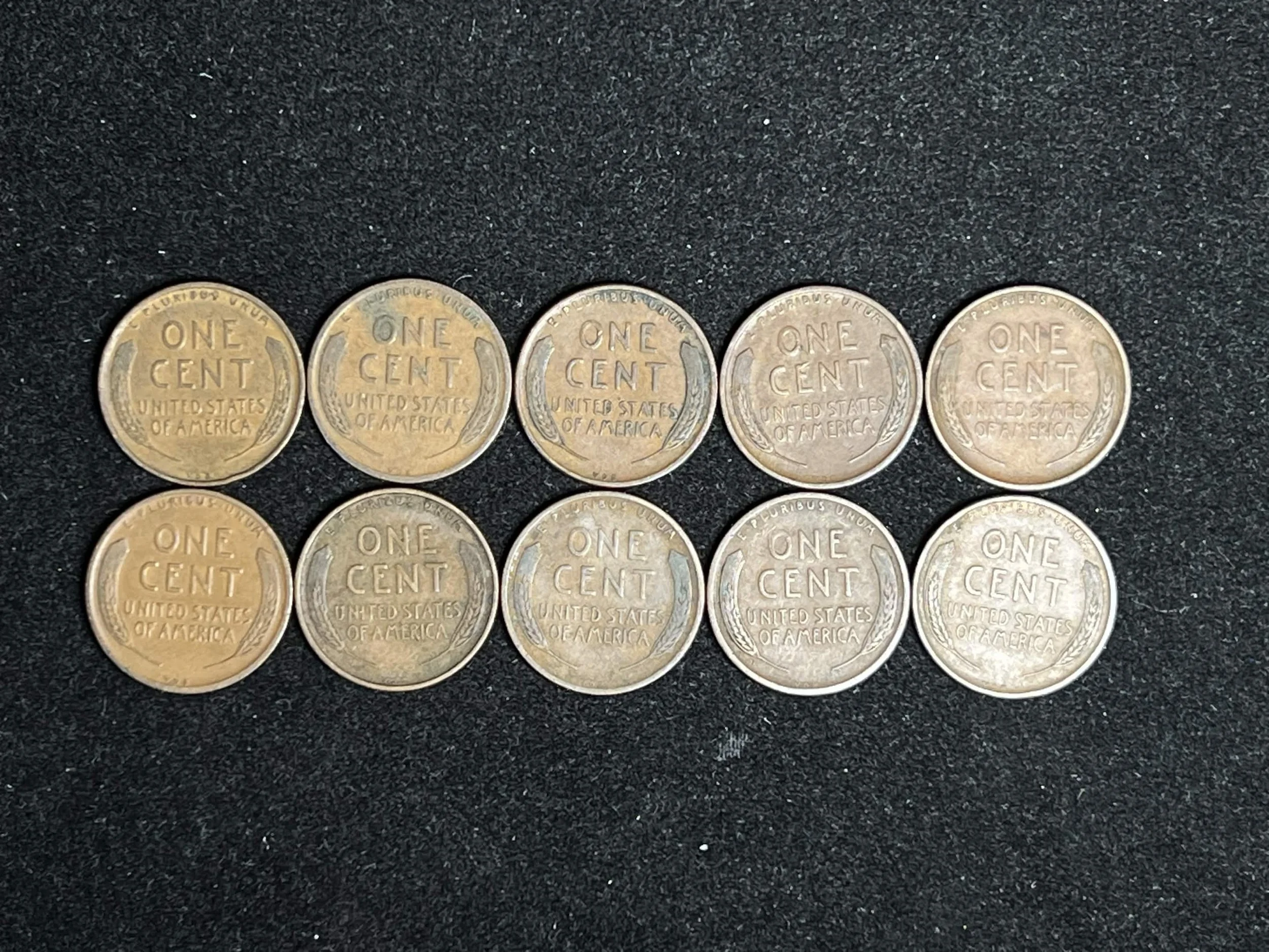 Line of five US one-cent coins on black surface, showing their reverse side.