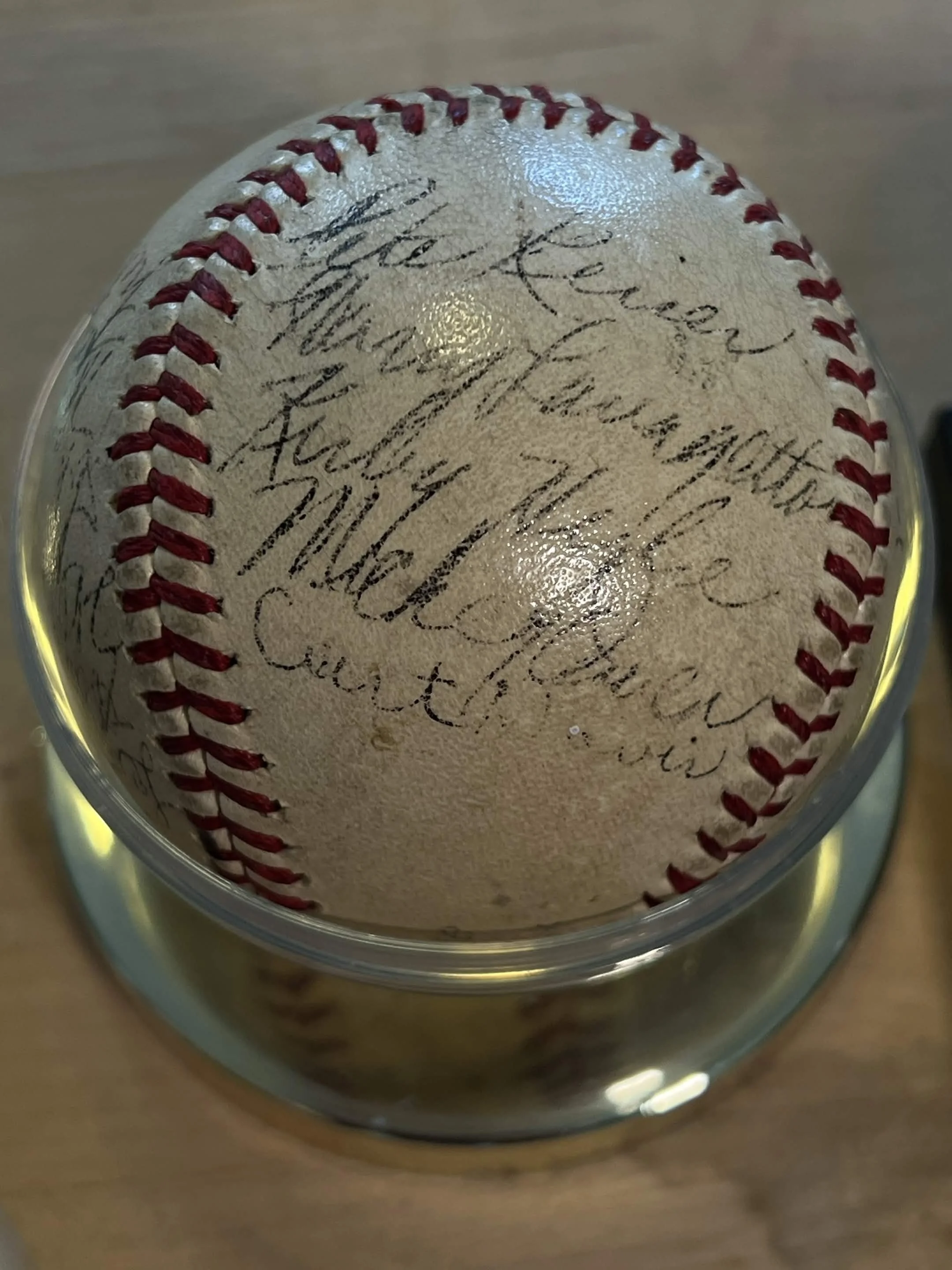 Close-up of a baseball with signature writing on its surface, inside a clear protective display case.