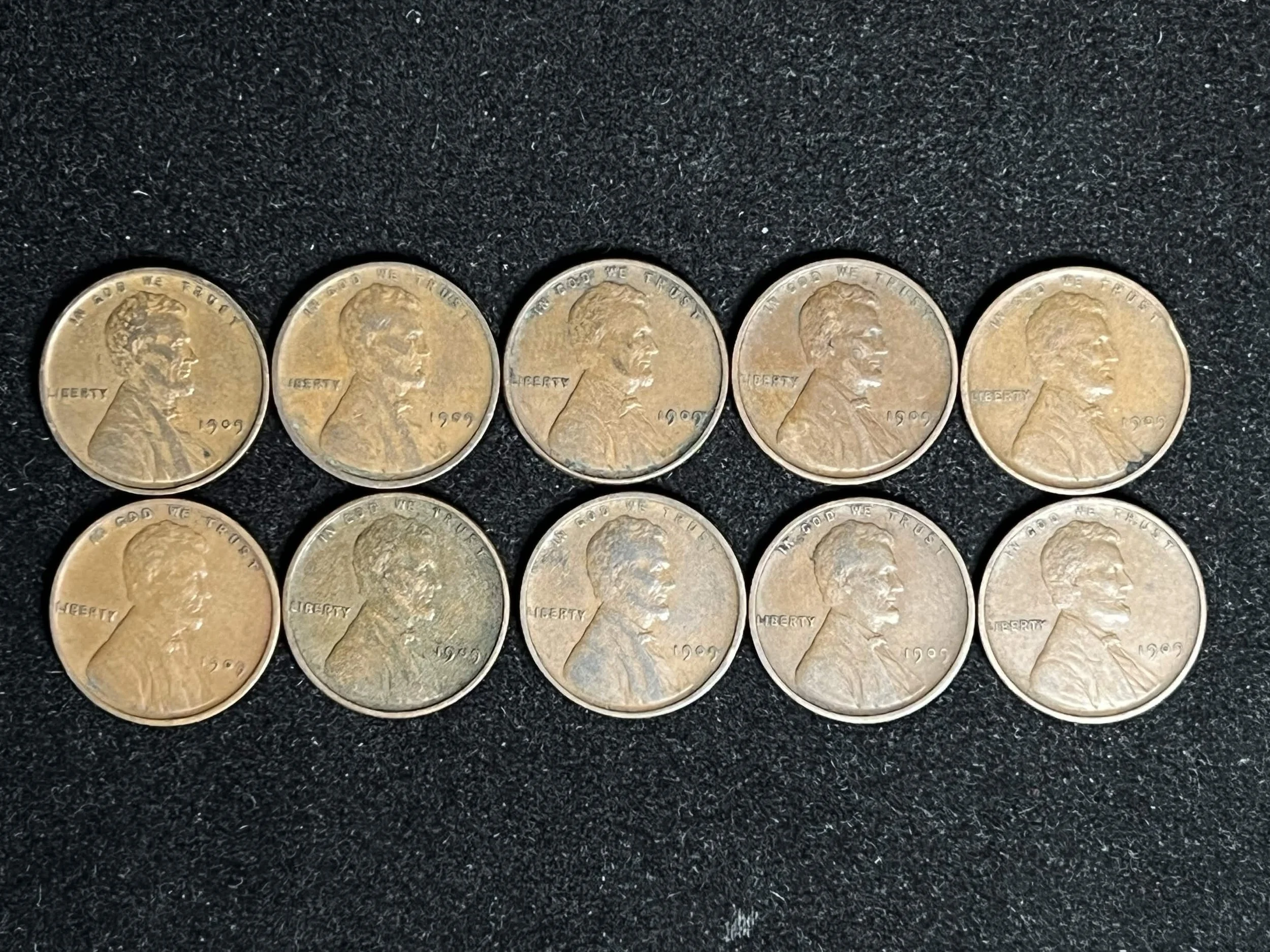 Six pennies placed side by side on a black textured surface.