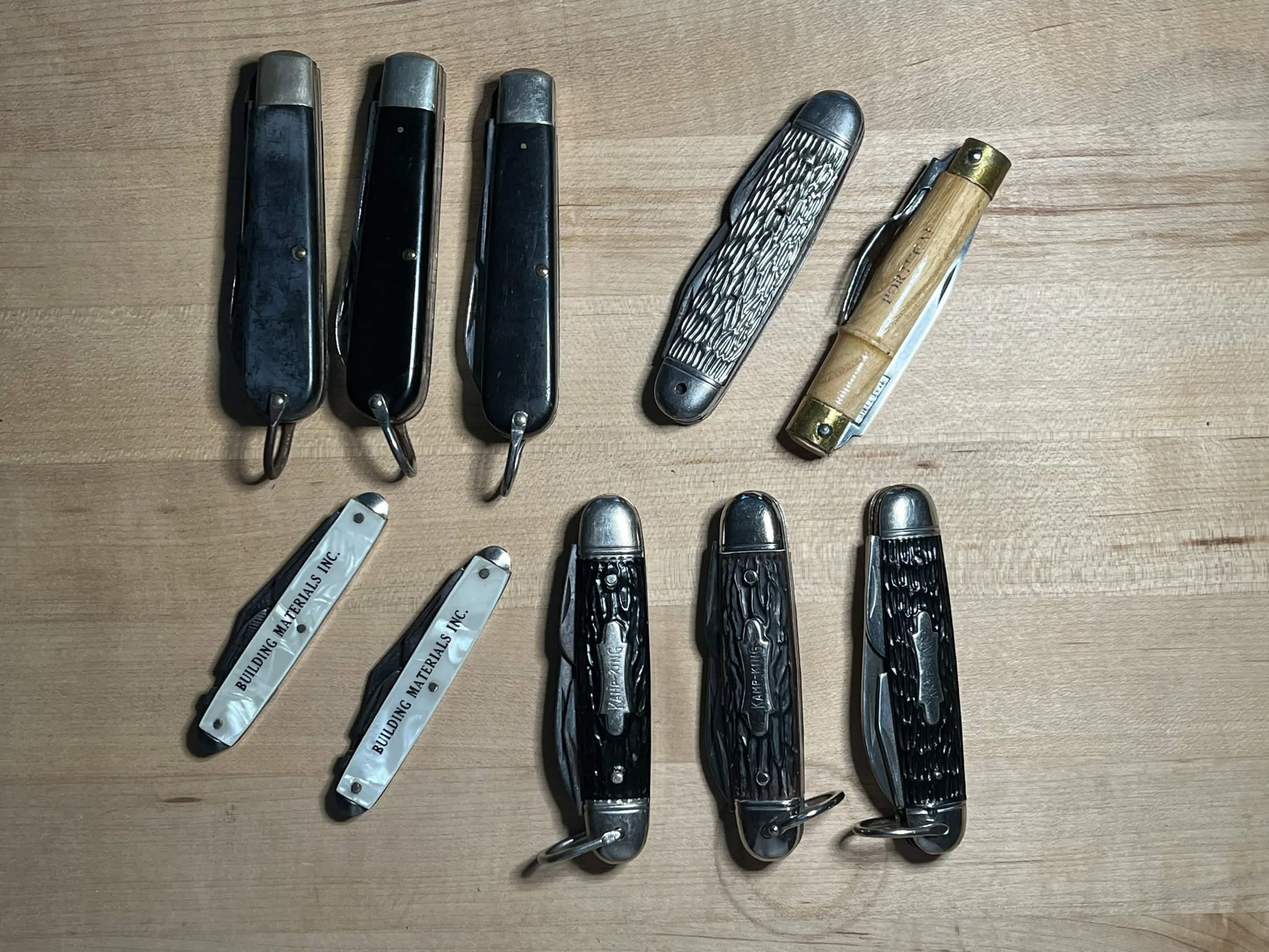 Collection of pocket knives with various handles laid out on a wooden surface.