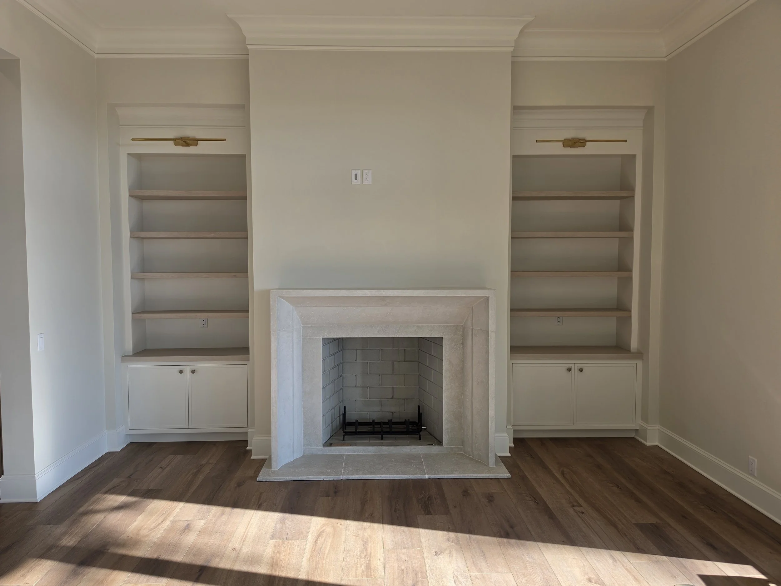 Empty living room with beige walls, built-in shelves, a fireplace, and hardwood floors.