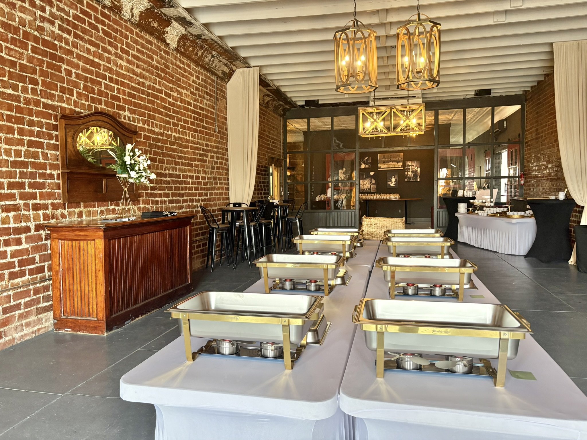 Interior of a restaurant with brick walls, modern lighting fixtures hanging from the ceiling, and tables set for dining, including a buffet table with various dishes.