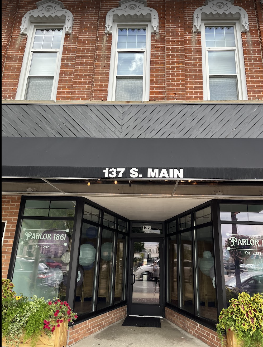 The entrance of a restaurant named Parlor 1861 at 137 S. Main, with large glass windows, potted flowers, and a black awning.