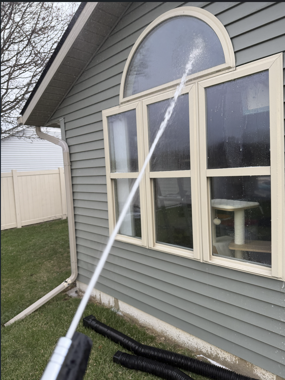A person using a pressure washer to clean the exterior of a house, focusing on the window area.
