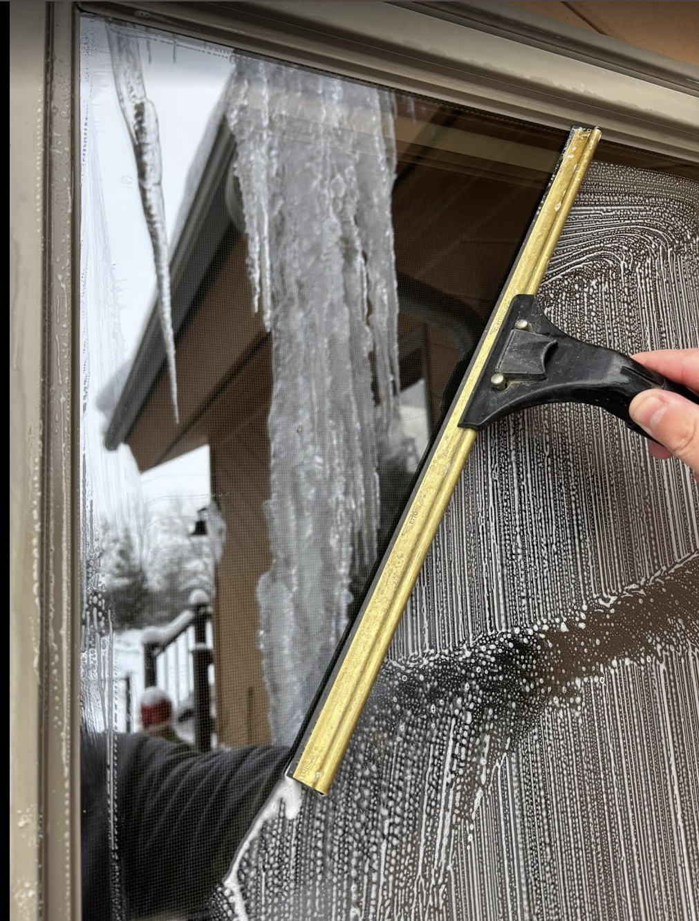 A person scrapes ice from a window with a squeegee on a cold day.