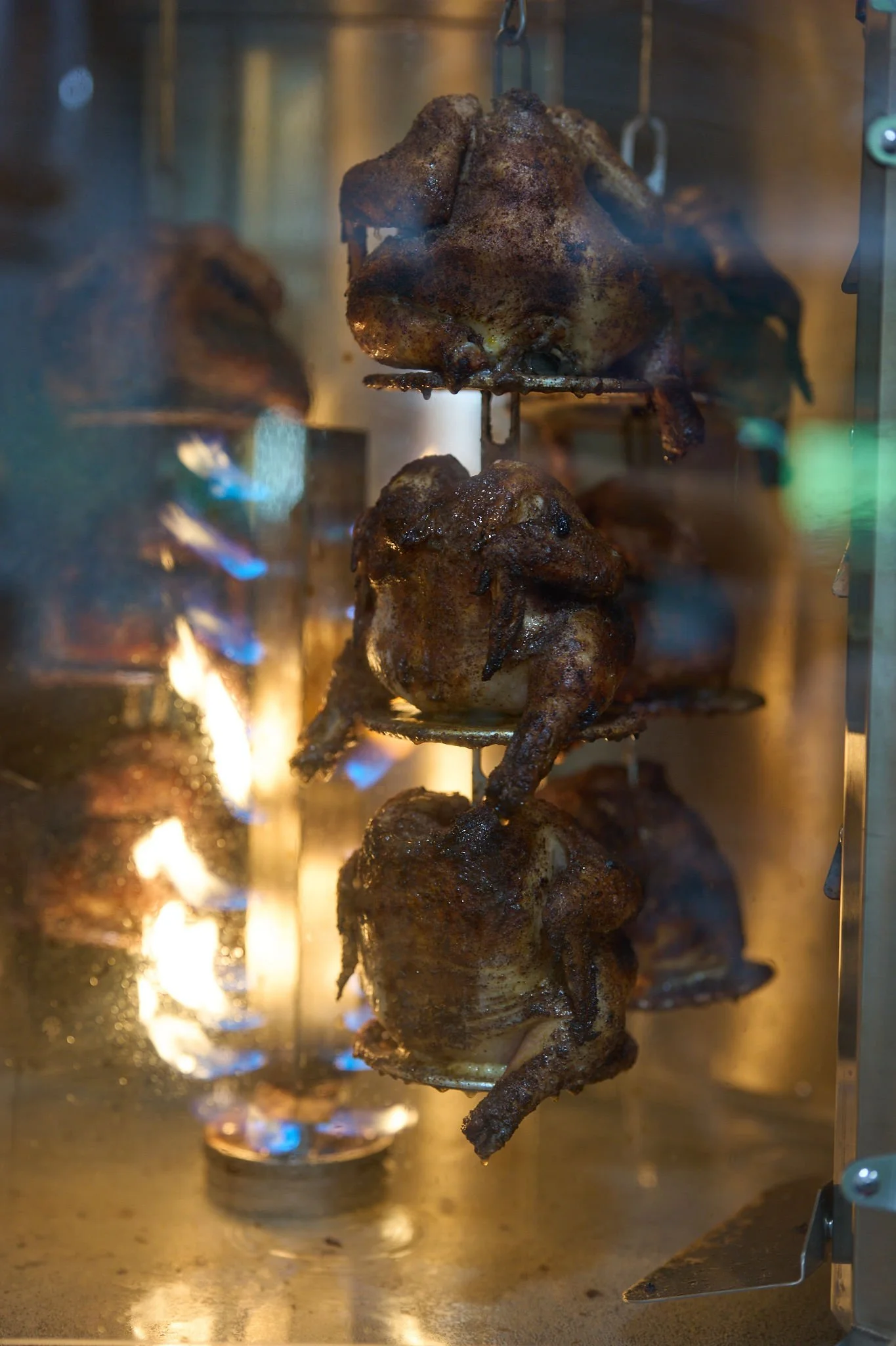 Multiple skewered grilled meat pieces cooking inside an oven with visible flames at the bottom.
