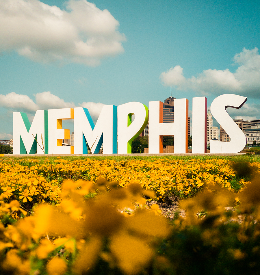Large sign spelling 'MEMPHIS' against a city skyline, with yellow flowers in the foreground and a partly cloudy blue sky.