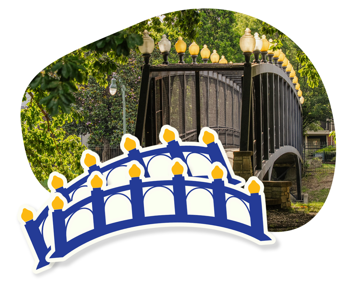 Photo of a black metal pedestrian bridge with ornate lamp posts on top, surrounded by green trees, with a decorative sticker of a blue and white bridge with yellow accents overlaid on it.