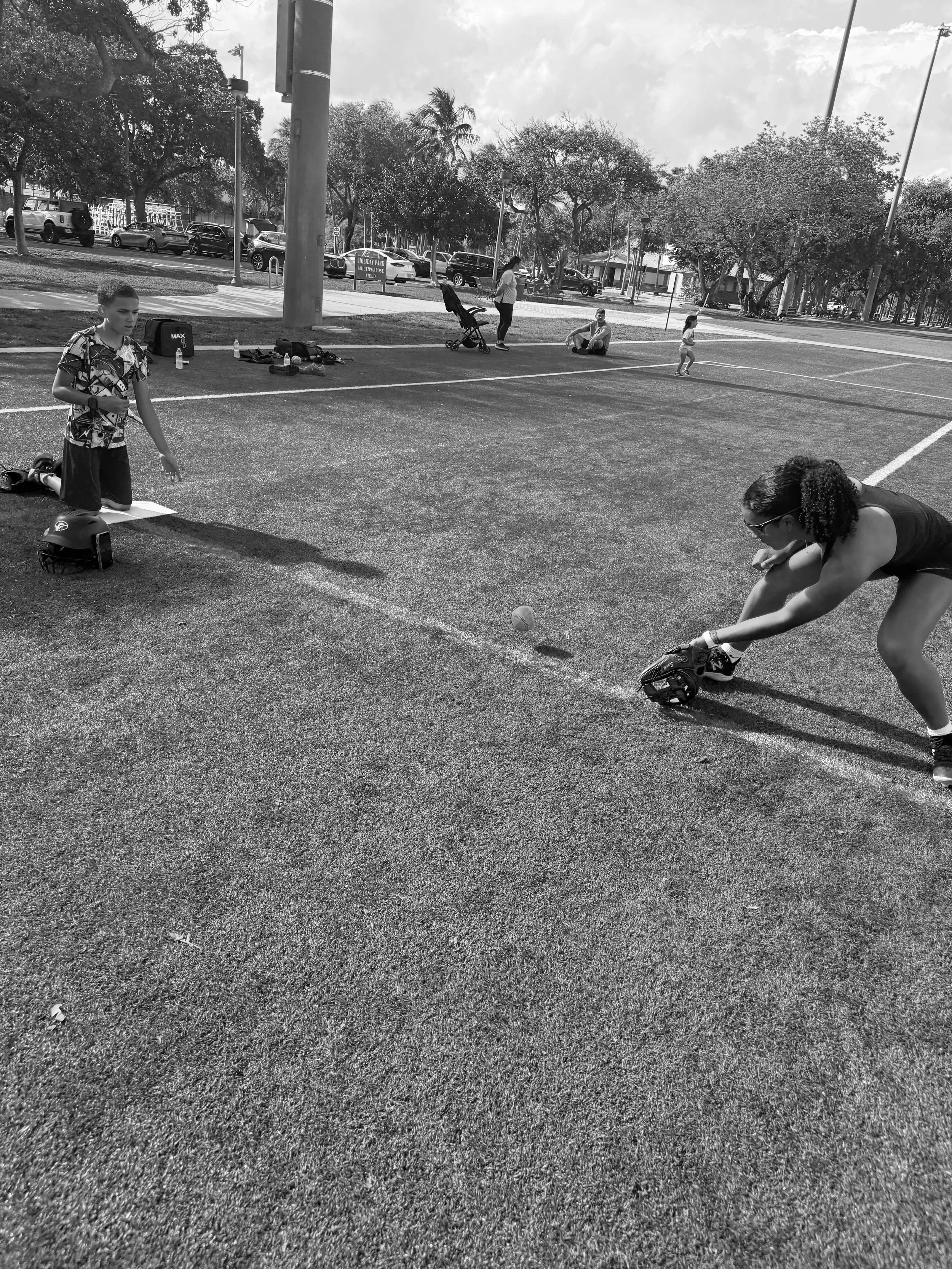 People playing cricket in a park on a sunny day.