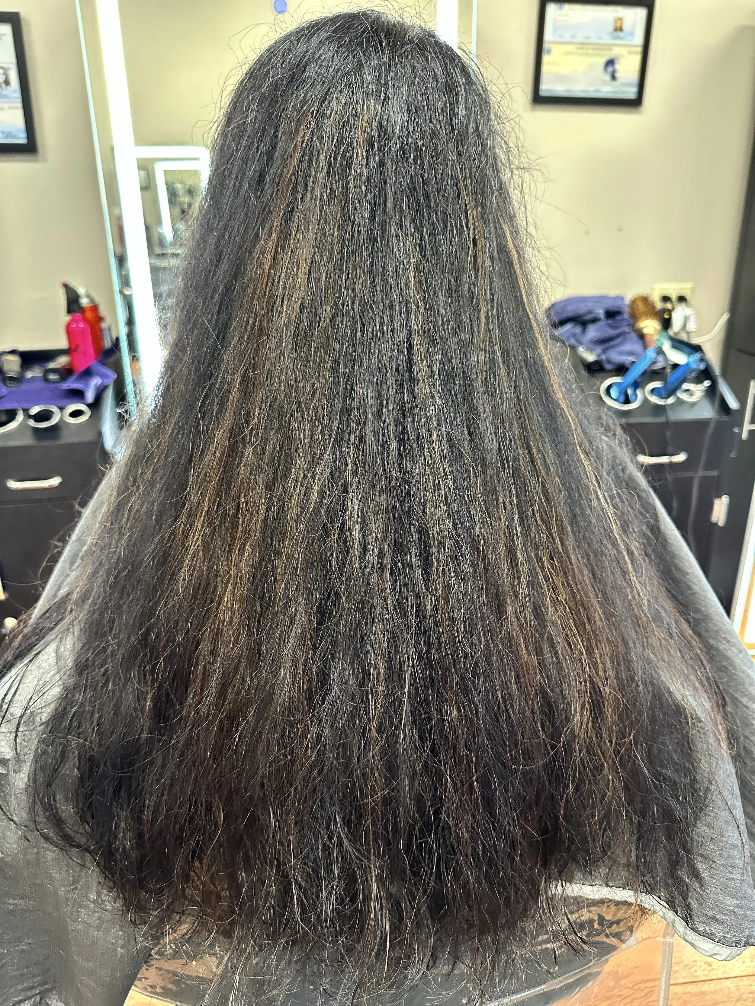 Back of a person with long, dark, slightly curly hair in a salon or barbershop.