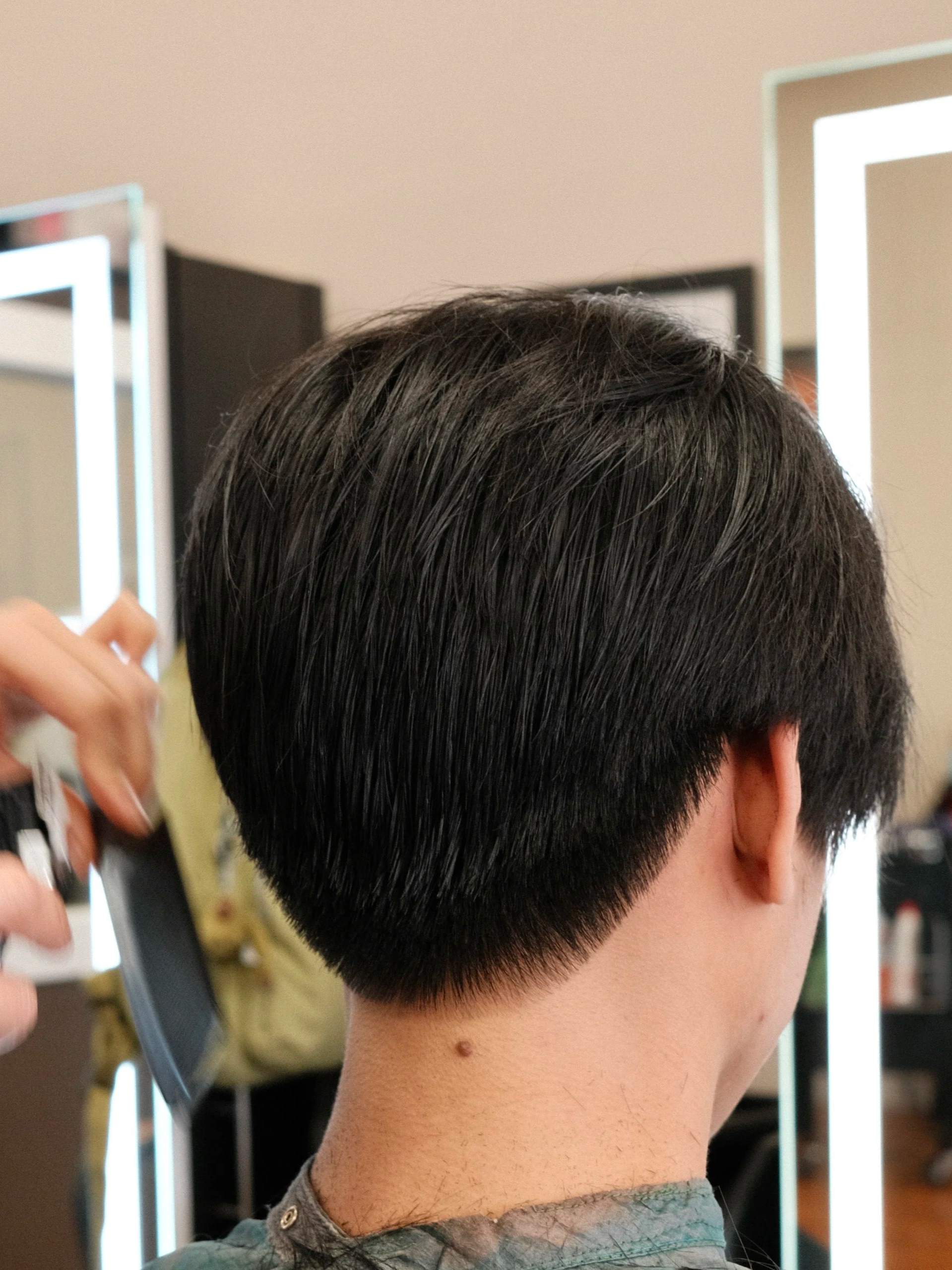 Person getting a haircut at a salon, with hairdresser using scissors, focus on back of person's head and hair.