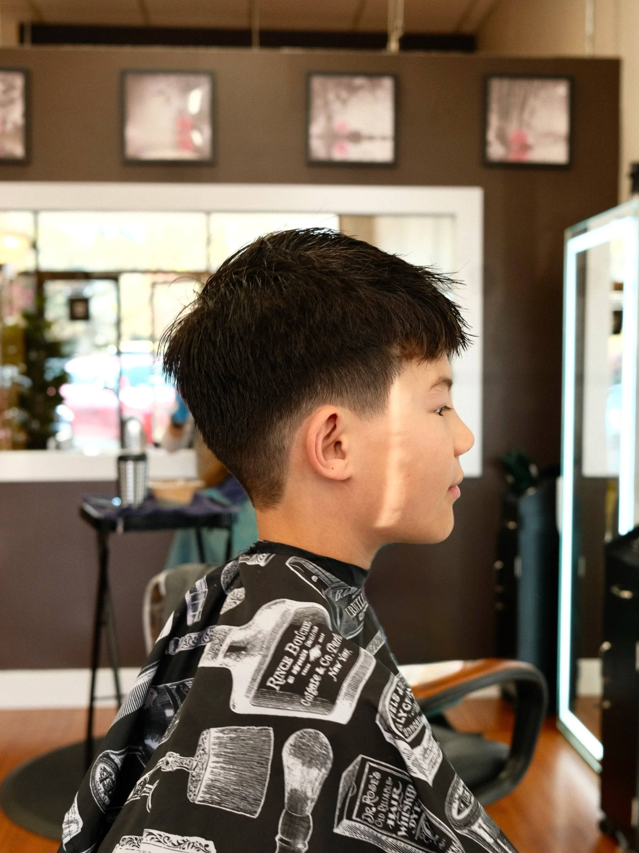 Side profile of a young boy with short dark hair sitting in a barber shop getting a haircut.