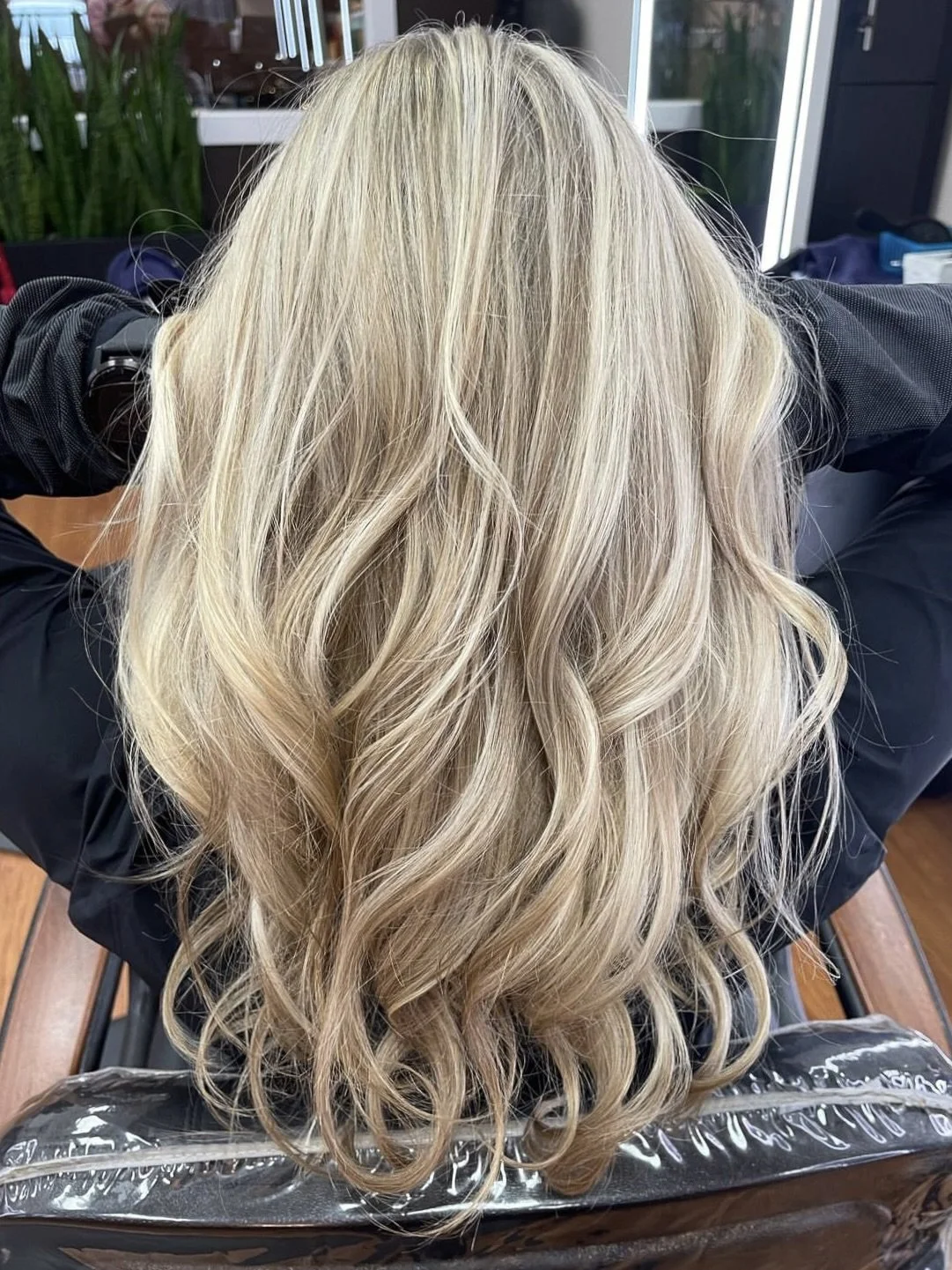 Back view of a woman with long, wavy, platinum blonde hair at a hair salon