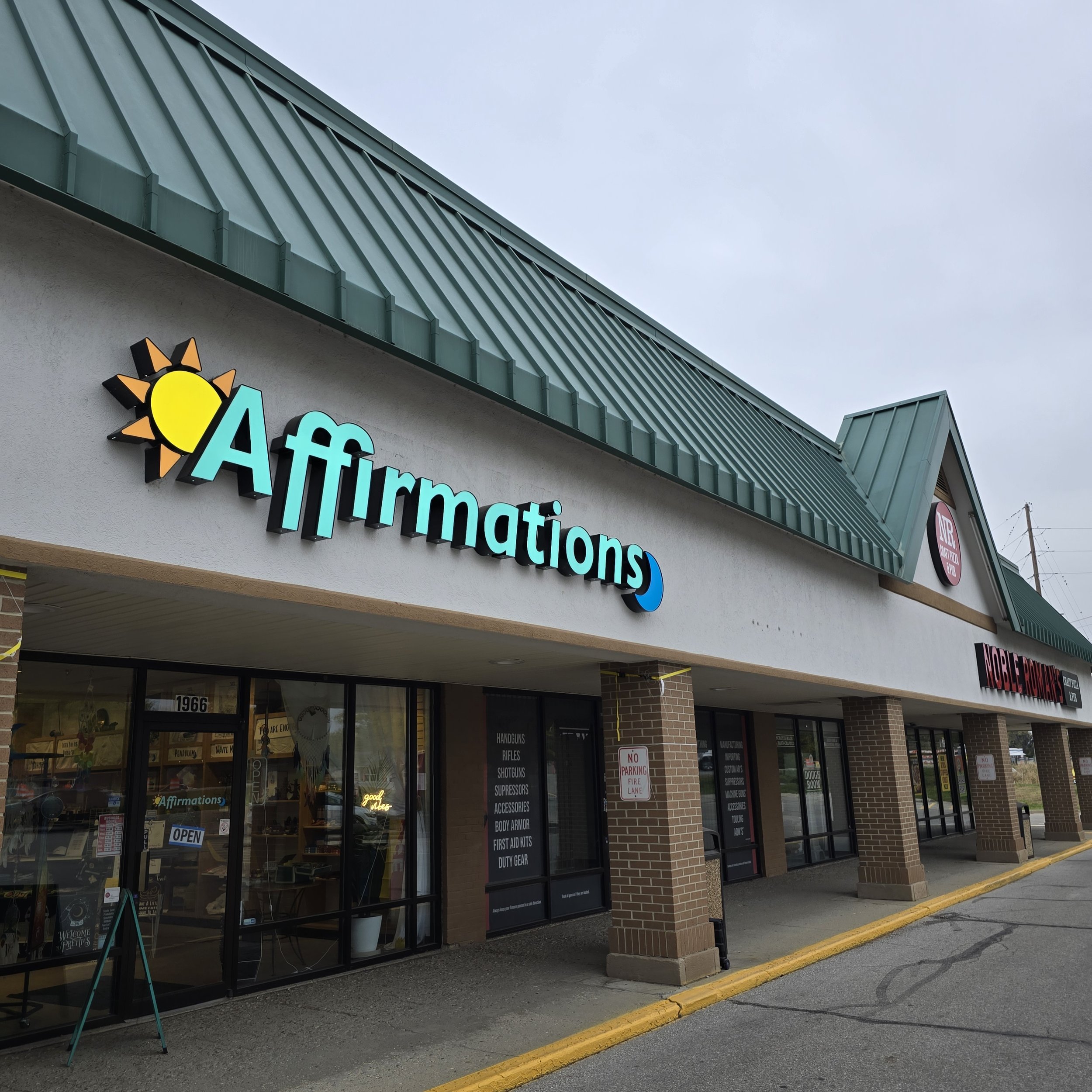 Outside view of Affirmations store with a partial store sign and large glass windows, a yellow parking curb, and a cloudy sky.