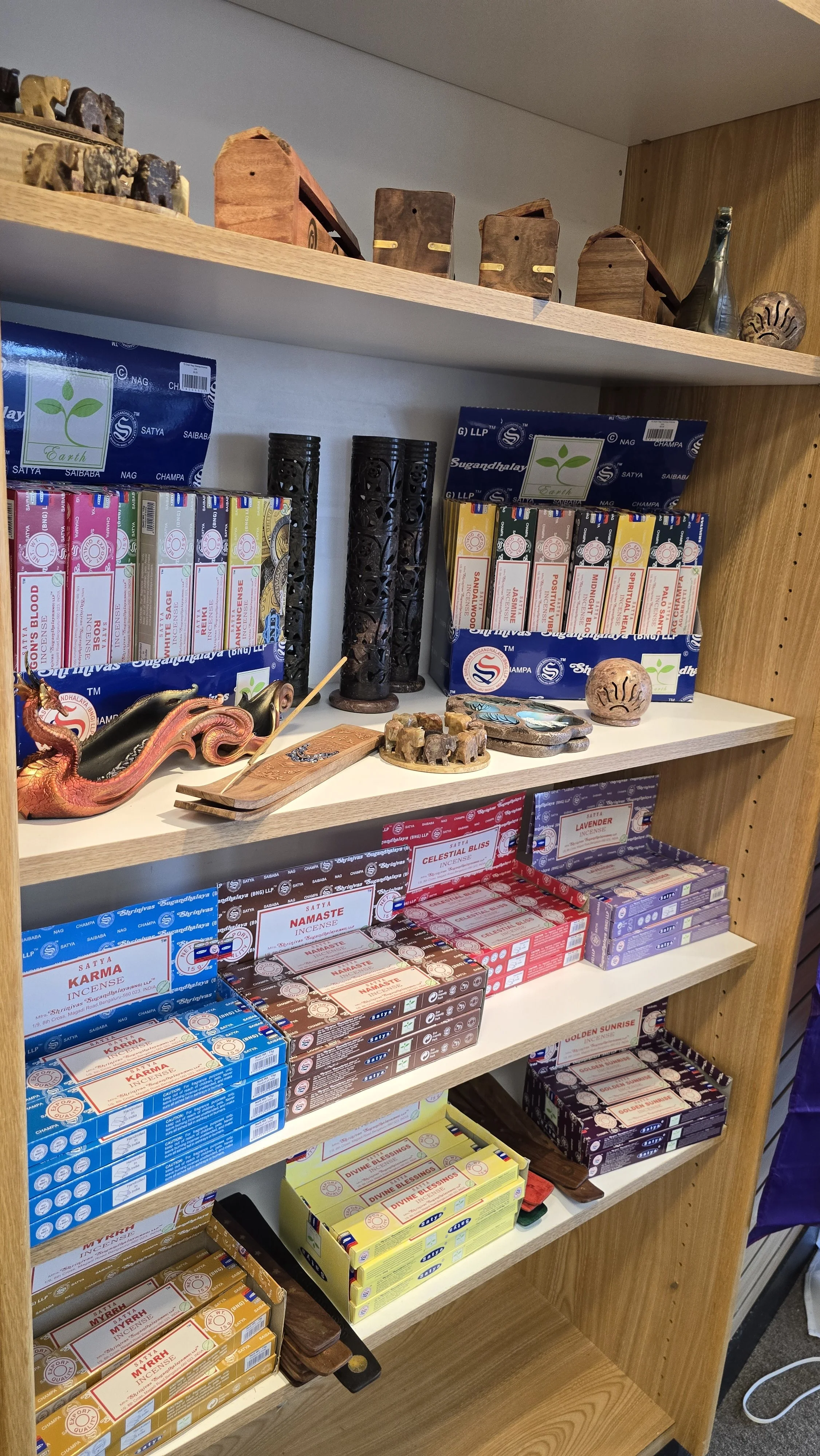 Wooden shelves stocked with various boxes of incense, decorative items, and small sculptures, including a dragon figurine and carved wooden pieces.