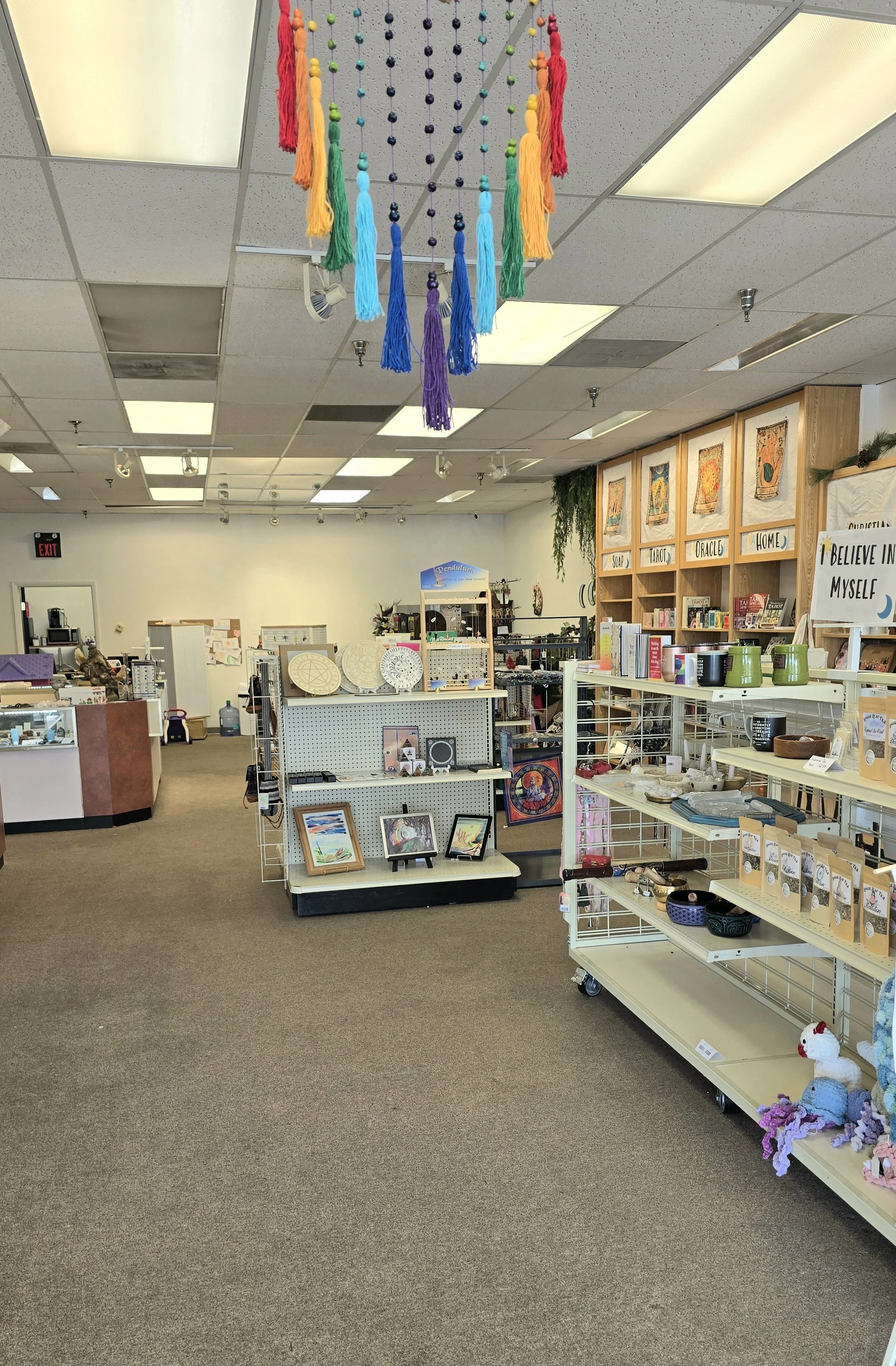 The interior of a gift shop or craft store with display shelves of artwork, pottery, and handmade crafts. There is a colorful feathered hanging decoration on the ceiling.