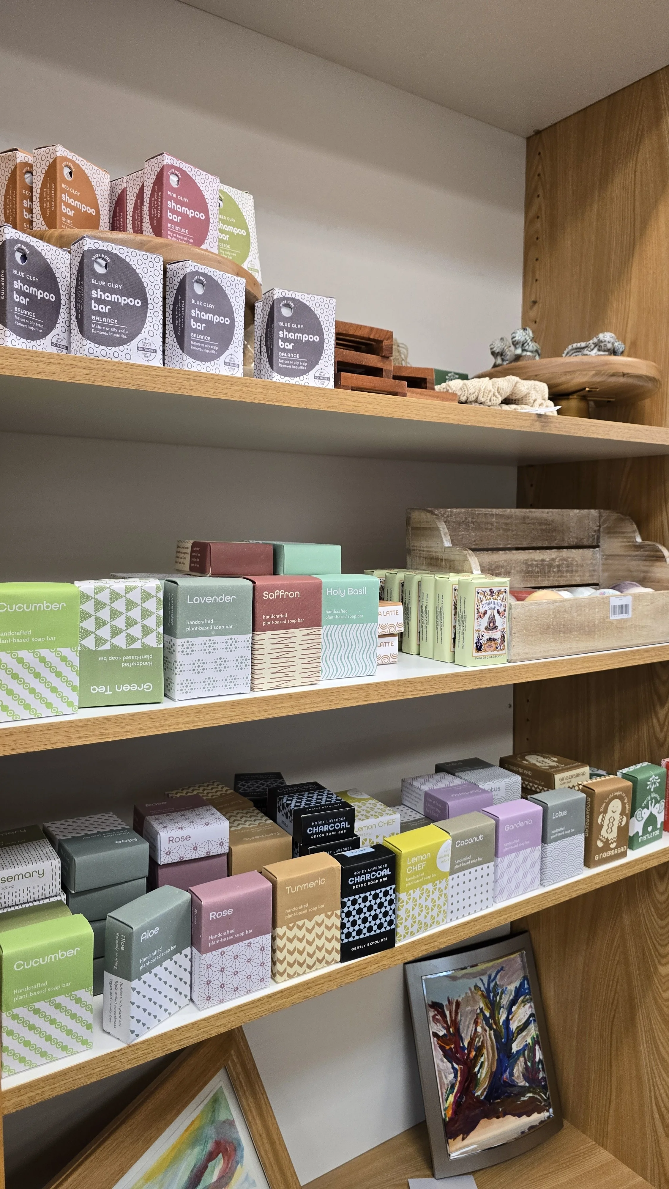 Wooden shelves displaying various colorful handmade soap bars, with artwork and decorative items nearby.