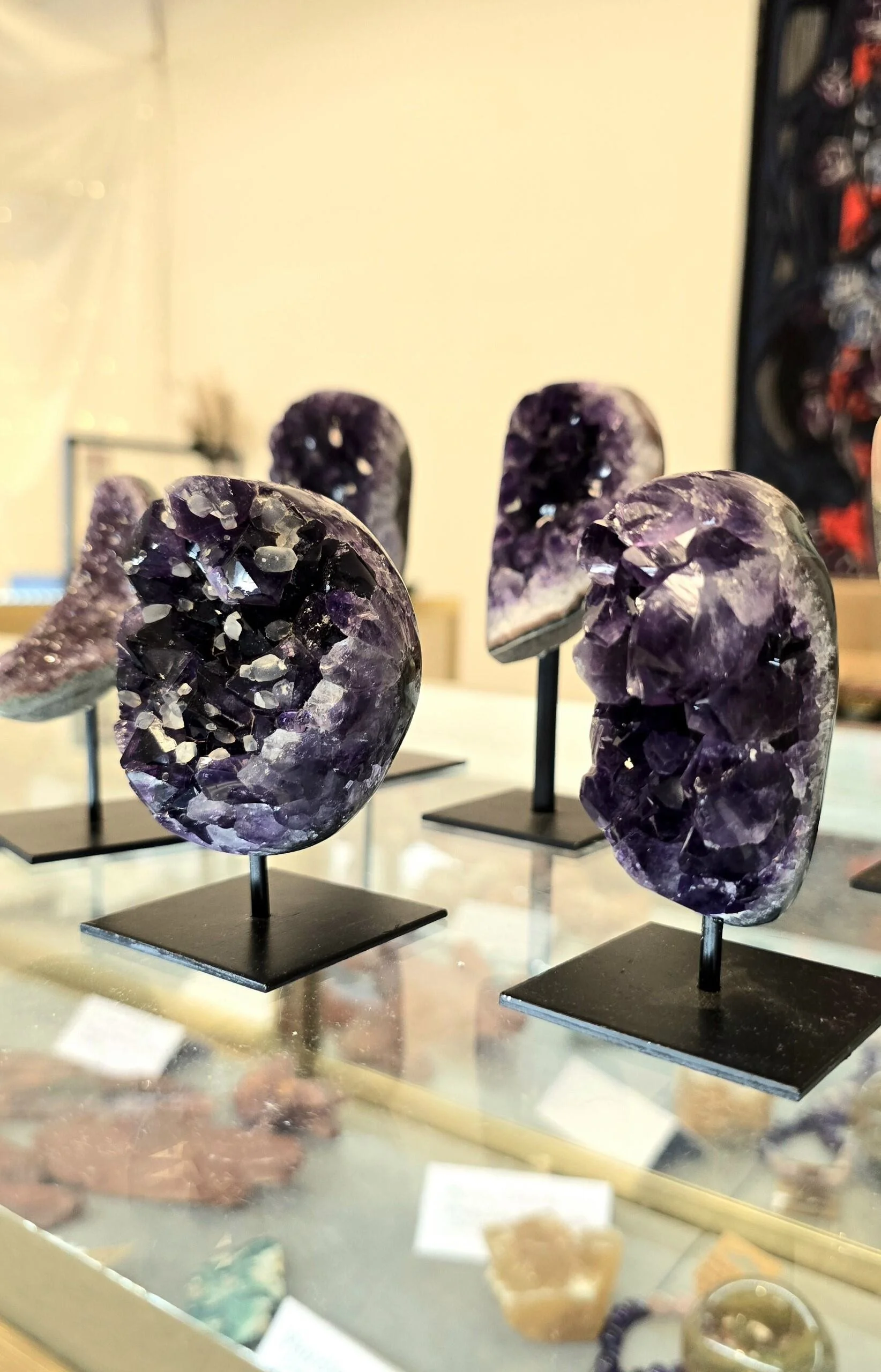 Display of several purple amethyst geode sculptures on black stands in a museum or exhibit display case.